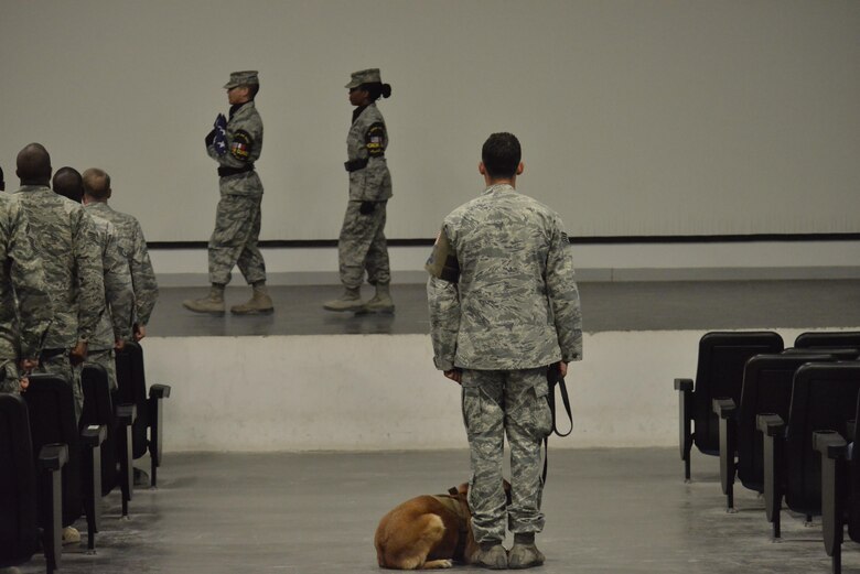 Ttilly, 379th Expeditionary Security Forces Squadron military working dog, sits next to her handler Staff Sgt. Jonathan Calo handler during the memorial service of MWD Jonny May 2, 2015 at the Blatchford-Preston Complex at Al Udeid Air Base, Qatar.  ( U.S. Air Force phot by Staff Sgt. Alexandre Montes)