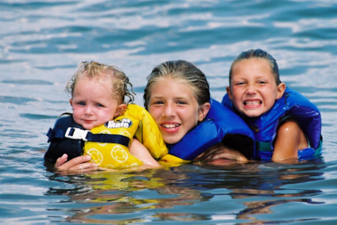 Three young visitors wading in the Thurmond Lake waters enjoying a swim safely wearing properly fitted lifejackets.