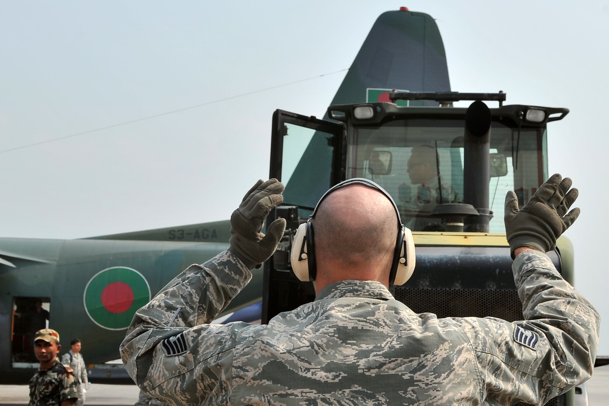 U.S. Air Force Tech. Sgt. Derrick McCall, 36th Mobility Response Squadron ramp coordinator, guides an Airman offloading relief supplies from a Bangladesh Air Force C-130 Hercules May 7, 2015, at the Tribhuvan International Airport in Kathmandu, Nepal. The Nepalese Army and Airmen worked with military members from the Bangladesh Air Force and Indian Air Force to process cargo from their aircraft arriving in Nepal to provide disaster relief following a magnitude 7.8 earthquake that struck the nation April 25. (U.S. Air Force photo by Staff Sgt. Melissa White/Released)