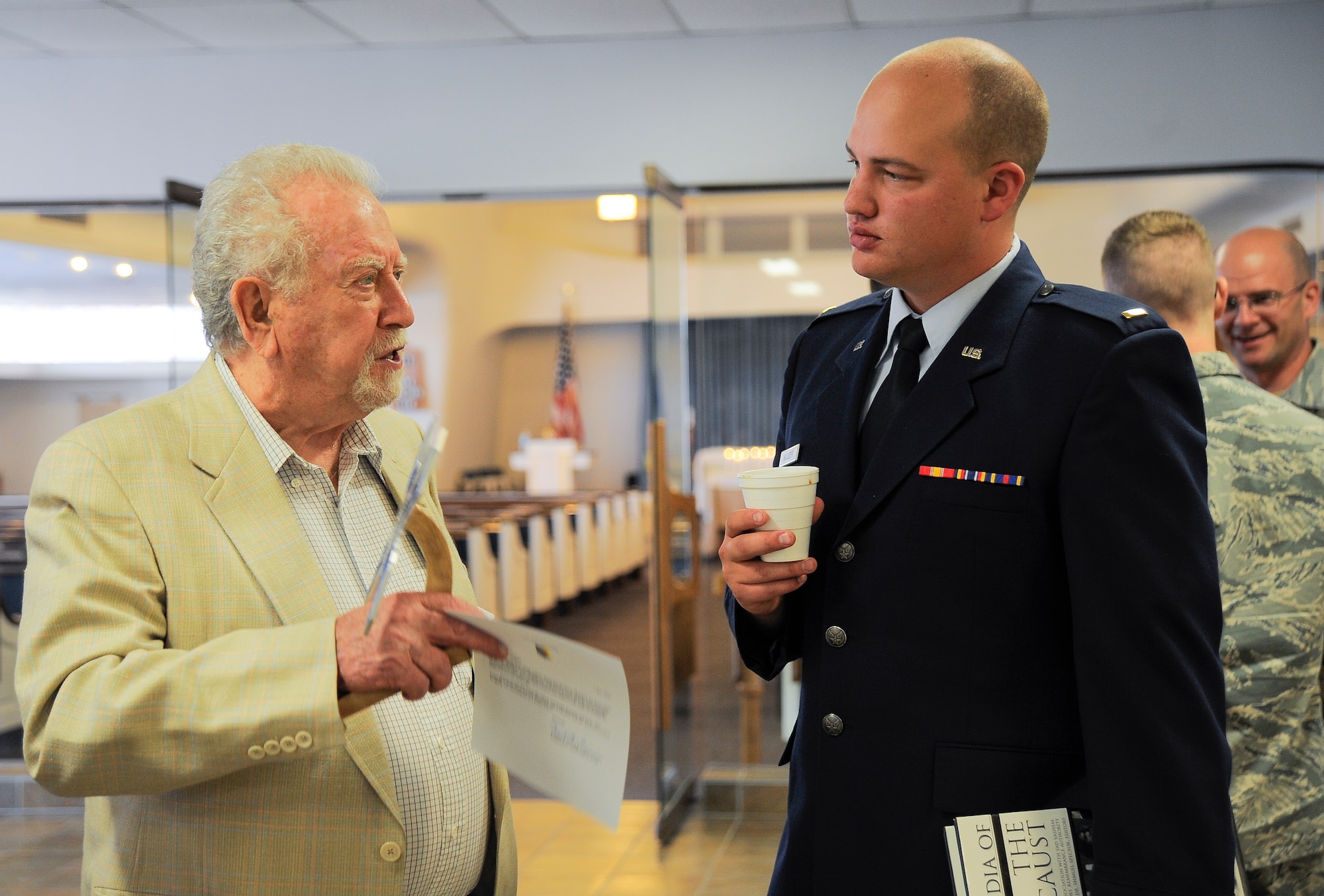 U.S. Air Force Pawel Linchter, Holocaust survivor, talks with 2nd  Lt Charles Hulsizer, 355th Force Support Squadron, following the Holocaust Day of Remembrance at Davis-Monthan Air Force Base, Ariz., May 7, 2015. Each of the Holocaust survivors was presented with a memento that created from the aircraft aluminum, shaped like a butterfly to represent freedom and hope. (U.S. Air Force photo by Staff Sgt. Angela Ruiz/Released) 