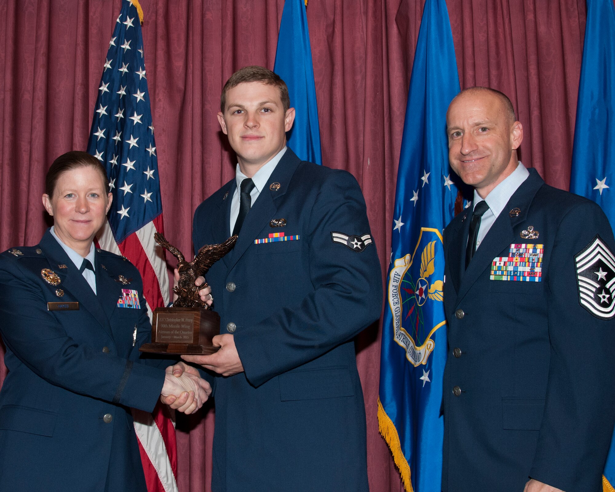 Airman 1st Class Christopher Perry, 90th Logistics Readiness Squadron, poses with Col. Tracey Hayes, 90th Missile Wing commander, and Chief Master Sgt. Samuel Couch, 90th MW command chief, at the 90th MW First Quarter Awards Breakfast, May 8, 2015, in the Trail’s End Club on F.E. Warren Air Force Base, Wyo. Perry won Airman of the Quarter for the wing. (U.S. Air Force photo by Senior Airman Jason Wiese)