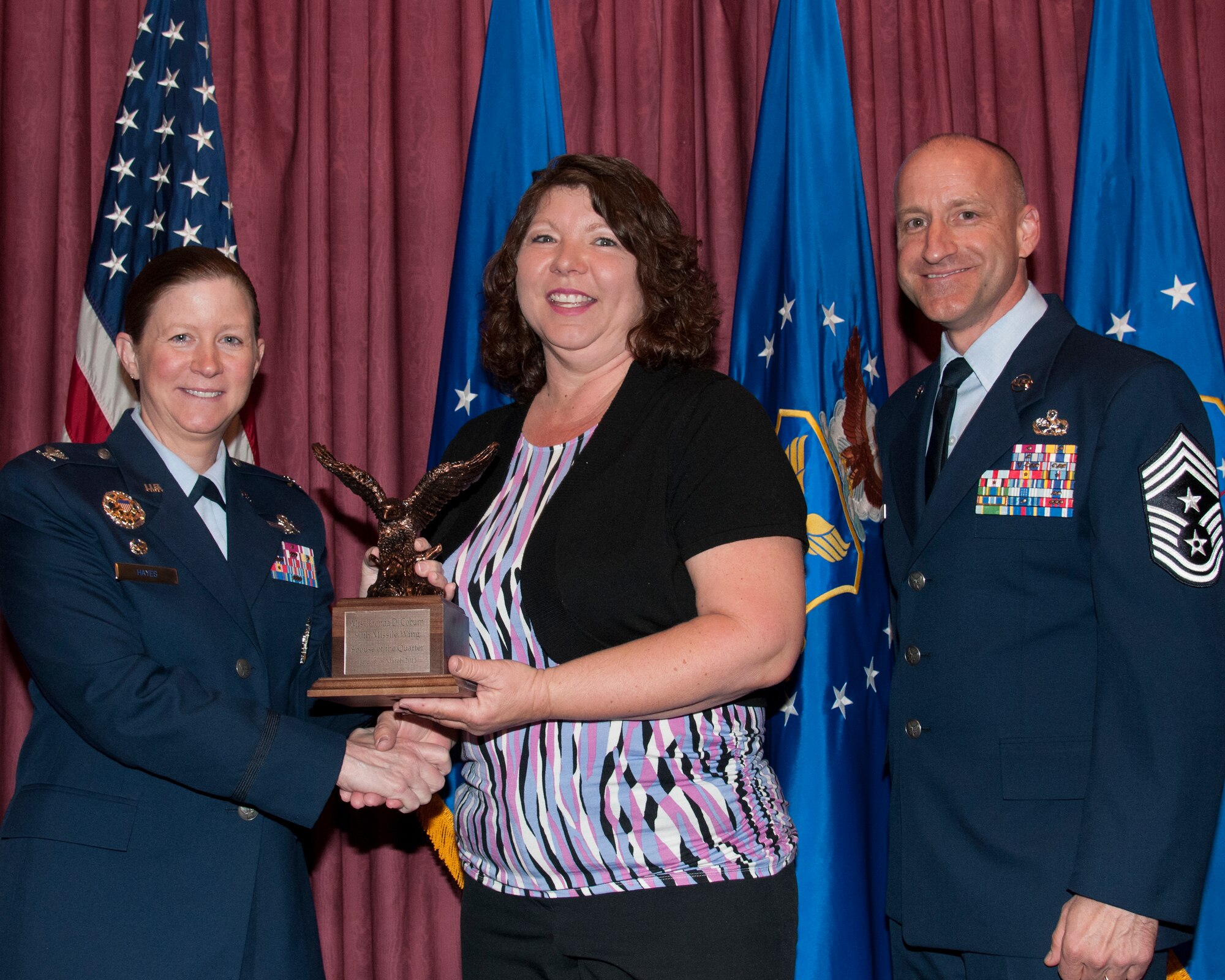Rhonda Coburn, wife of Chaplain (Maj.) Gary Coburn, 90th Missile Wing, poses with Col. Tracey Hayes, 90th MW commander, and Chief Master Sgt. Samuel Couch, 90th MW command chief, at the 90th MW First Quarter Awards Breakfast, May 8, 2015, in the Trail’s End Club on F.E. Warren Air Force Base, Wyo. Rhonda Coburn won Spouse of the Quarter for the wing. (U.S. Air Force photo by Senior Airman Jason Wiese)