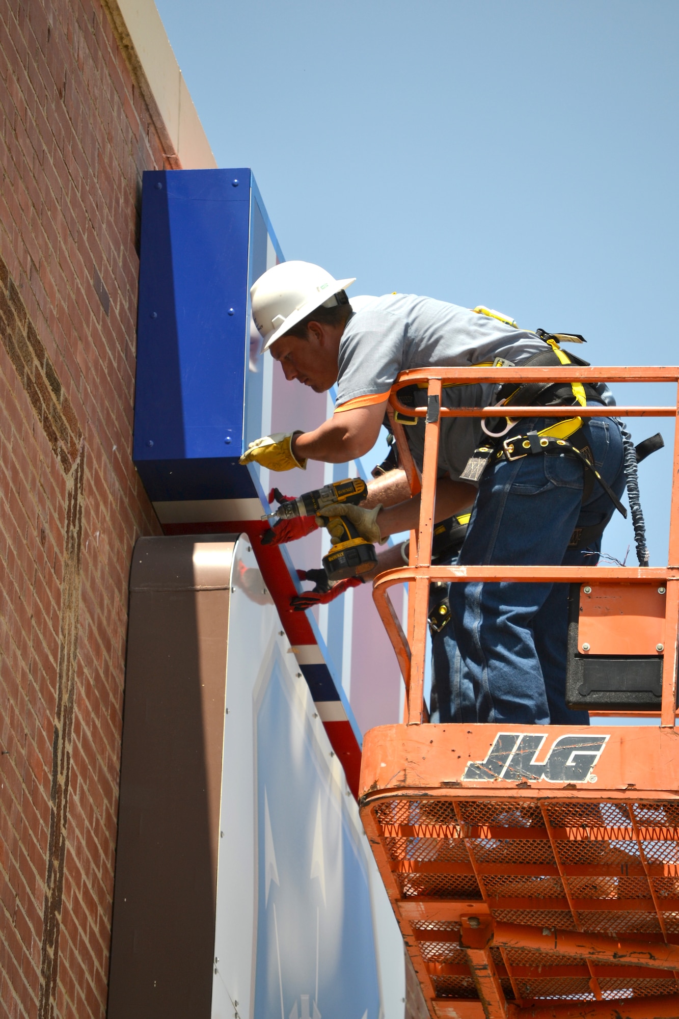 Dallas McCain, a maintenance carpenter with Tinker support services, attaches screws to the Air Force Organizational Excellence Ribbon on the front of Bldg. 3001. (Air Force photo by Ron Mullan/Released)