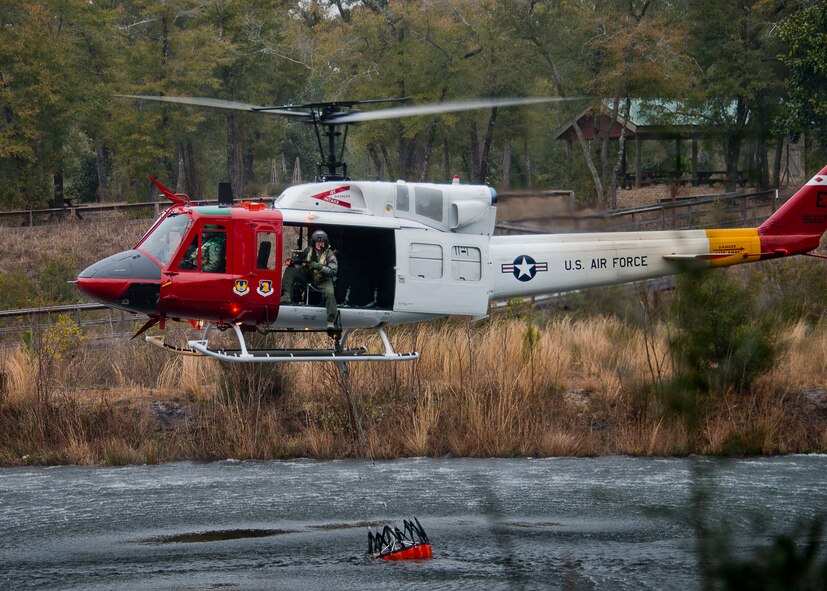 A 413th Flight Test Squadron UH-1 Huey gathers up a bucket of water from Anderson Pond during a training mission at Eglin Air Force Base, Fla.  The water bucket operations training is required for flight crews to maintain their firefighting proficiencies.  The 413th helicopters can be tasked by the 96th Test Wing to support Jackson Guard with fire management.  They supported a firefighting effort during a range fire North of Hurlburt Field in May 2012. (U.S. Air Force photo/Samuel King Jr.)