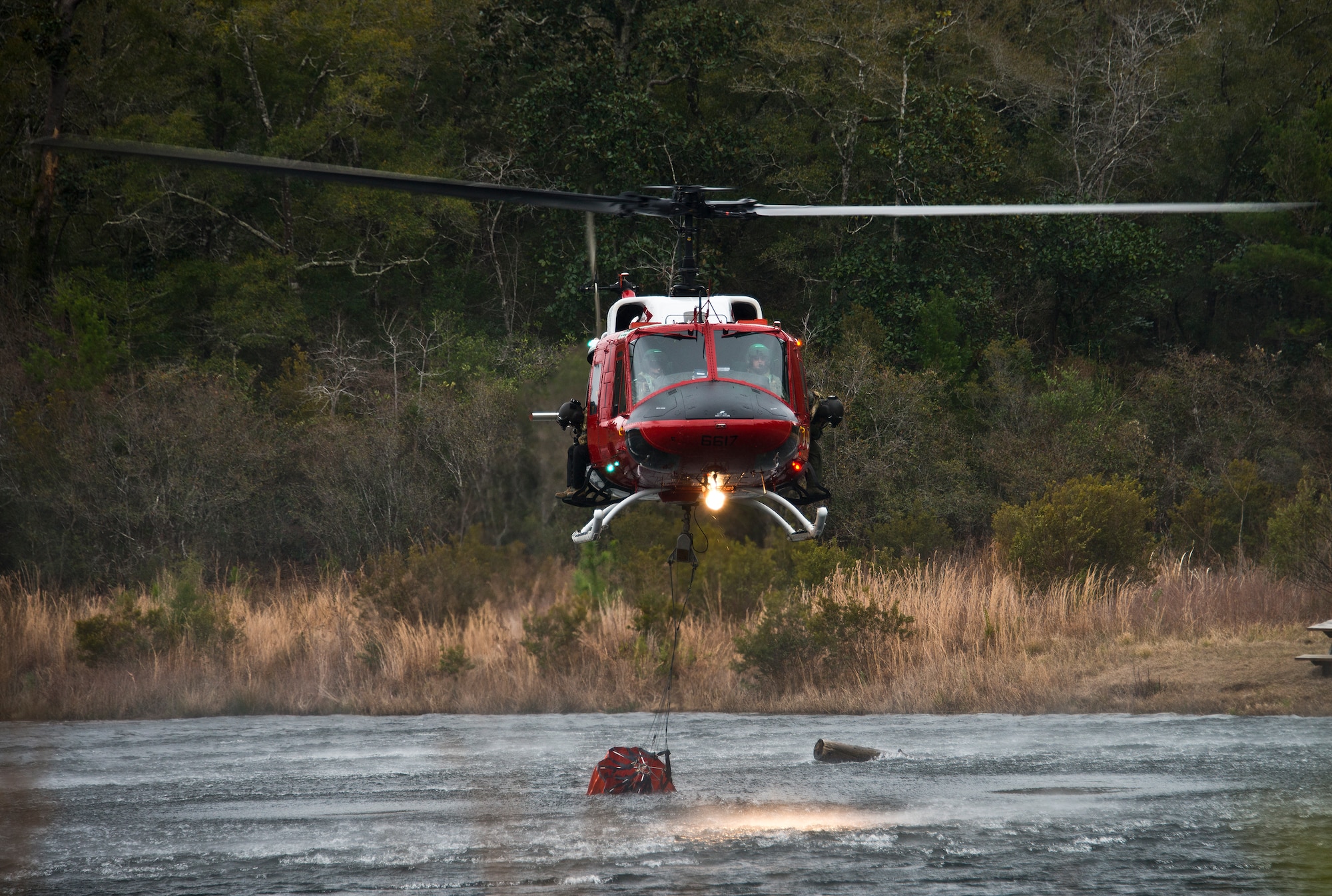A 413th Flight Test Squadron UH-1 Huey gathers up a bucket of water from Anderson Pond during a training mission at Eglin Air Force Base, Fla.  The water bucket operations training is required for flight crews to maintain their firefighting proficiencies.  The 413th helicopters can be tasked by the 96th Test Wing to support Jackson Guard with fire management.  They supported a firefighting effort during a range fire North of Hurlburt Field in May 2012. (U.S. Air Force photo/Samuel King Jr.)