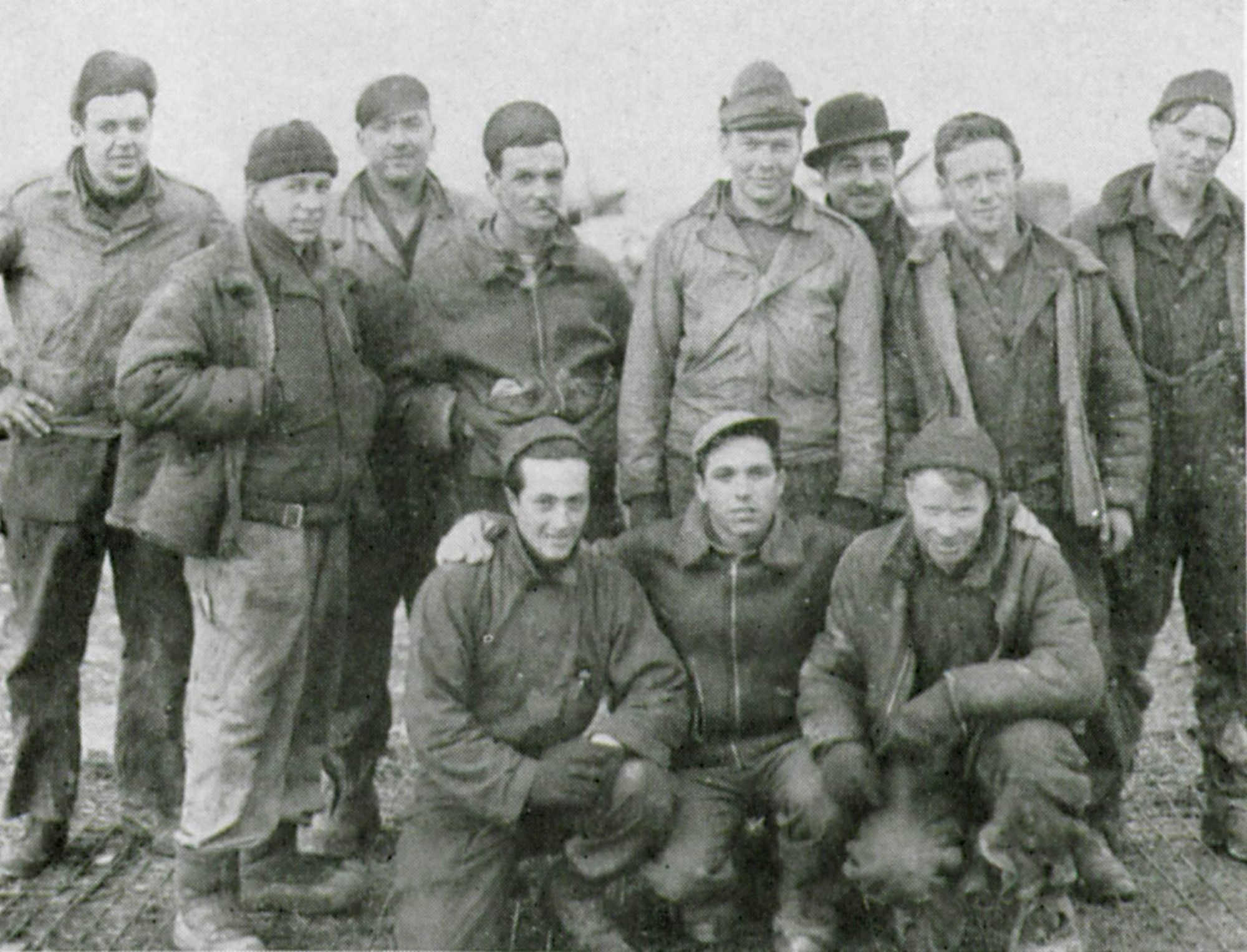 Enlisted men of the 405th Fighter Squadron who kept their Thunderbolts going in all kinds of conditions assemble for a flightline picture at a rugged airfield during some miserable winter weather.  Shown are their final wartime ranks.  Standing from left to right are S/Sgt John S. Piotrowski, Sgt. Donald E. Wright, S/Sgt Conrad M. Shelley, Sgt. Paul S. Kikta, T/Sgt William A. Morrison, S/Sgt Joseph L. Guarin, S/Sgt Francis T. Parker, Sgt. John J. Desmond.  Kneeling left to right are Sgt. Nicholas T. Mistretta, Cpl. Anthony J. Tenore and Sgt. Pearle S. Johnson. (The Story of the 371st Fighter Group in the E.T.O.)