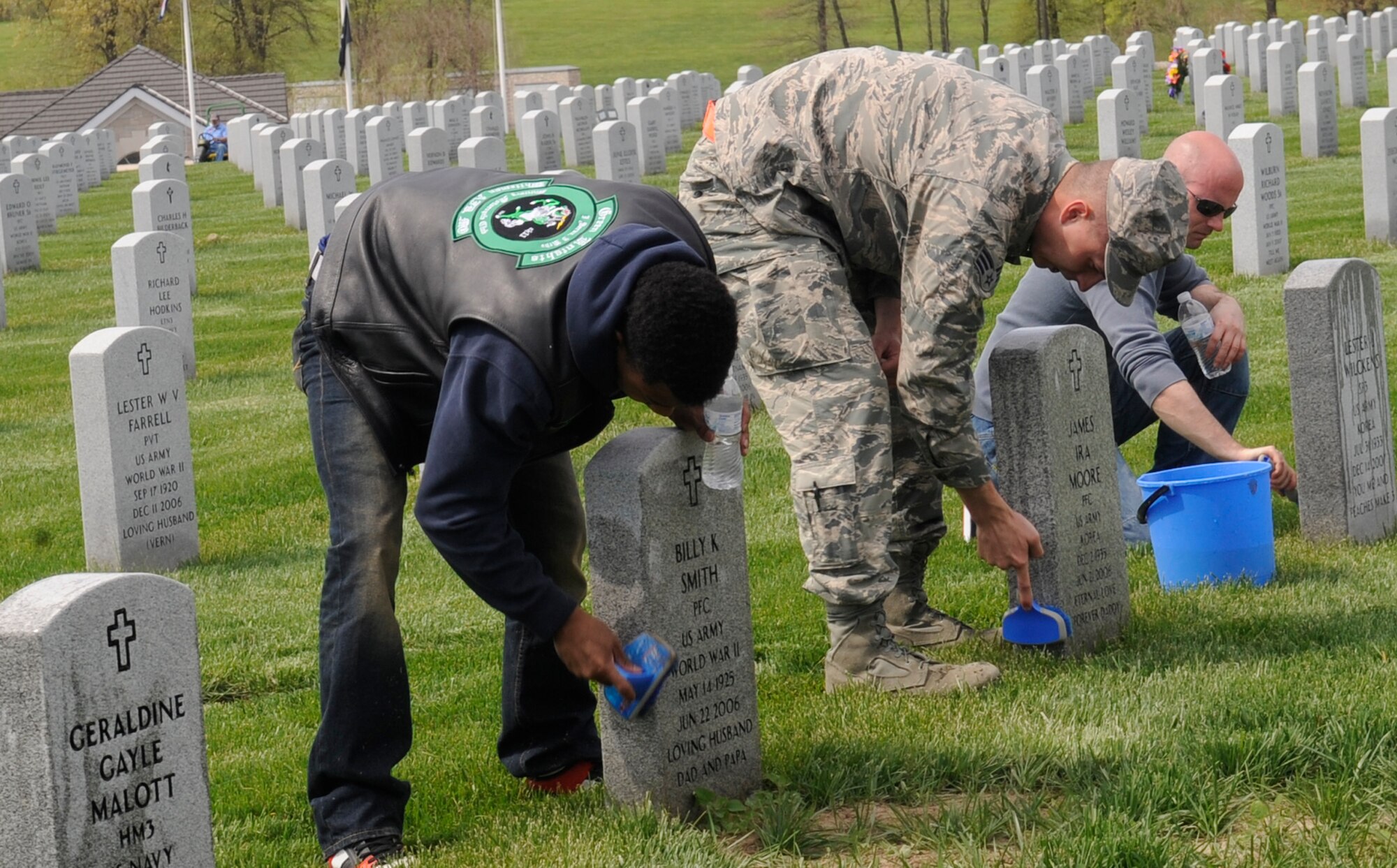 Senior Airman Armond Dinett, 509th Maintenance Squadron, signature diagnosis journeyman, Tech. Sgt. Joel Sneddy, 509th MXS low observable craftsman, and Senior Airman Shane Smith, 509th Aircraft Maintenance Squadron administration assistance, scrub headstones of dirt at the Missouri Veterans Cemetery at Higginsville, Mo., April 27, 2015. More than 35 riders participated in the mentorship ride to the cemetery. (U.S. Air Force photo by Staff Sgt. Alexandra M. Longfellow/Released)