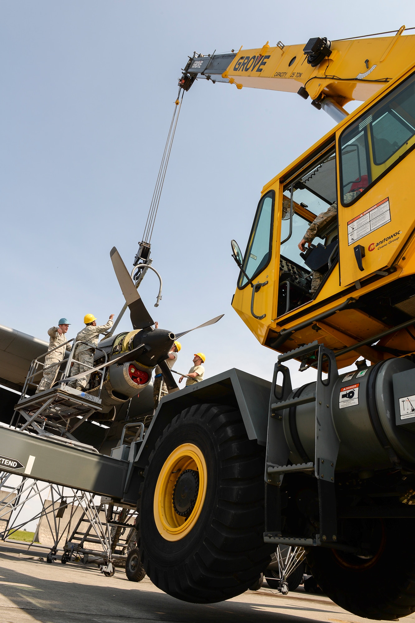Crewmembers of the 374th Maintenance Squadron and the 374th Air Maintenance Squadron coordinate with a crane operator with the 374th Civil Engineer Squadron to secure the crane to a C-130 Hercules engine, April 29, 2015 at Yokota Air Base, Japan. After maintainers harnessed the engine, the crane operator lifted the engine off its wing and lowered it to the ground. (U.S. Air Force photo by Airman 1st Class Elizabeth Baker/Released)