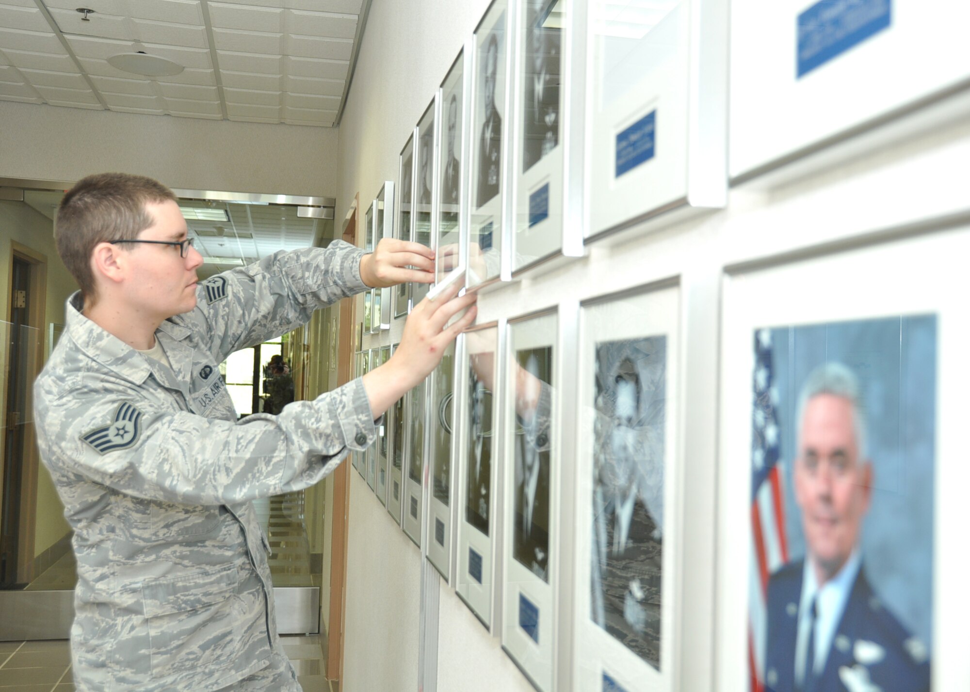 Staff Sgt. Benjamin Herrington, 940th Wing historian, uses a level when setting up a new photo display in the wing headquarters building, May 3, Beale Air Force Base, California. Herrington gathered 23 photos of past commanders, starting from 1963 to present day, to showcase the wing’s heritage. (U.S. Air Force photo/Tech. Sgt. Heather Skinkle)
