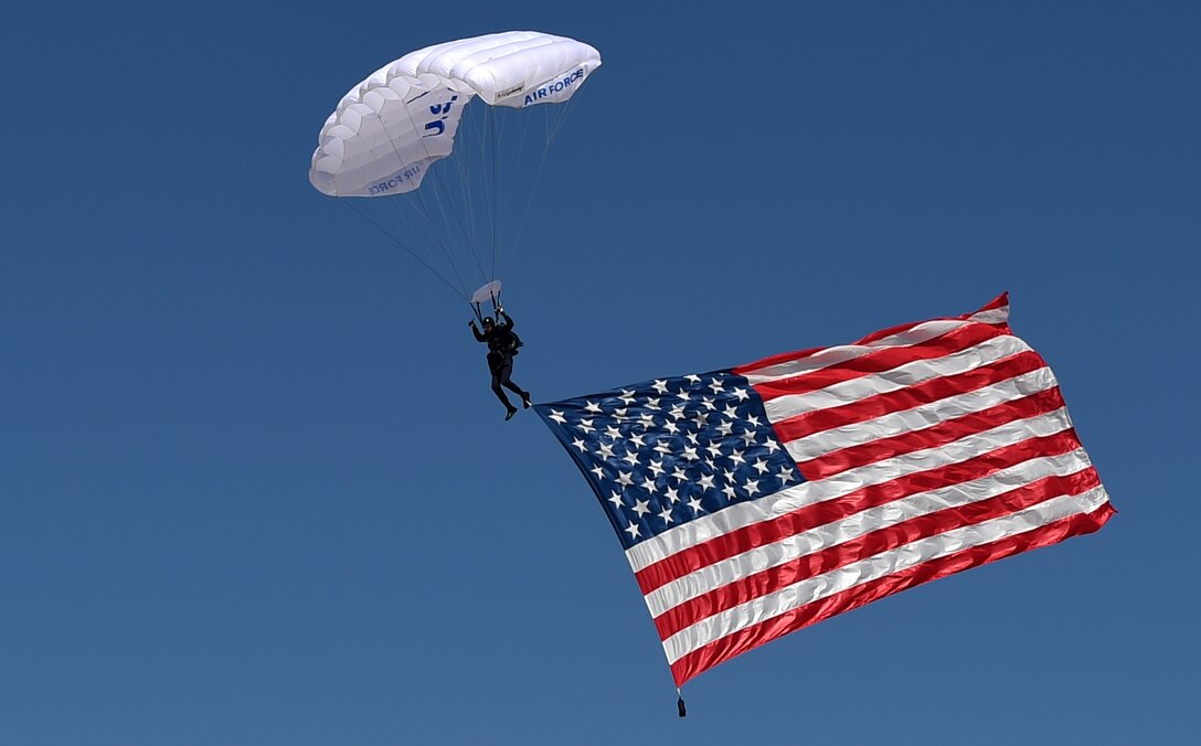 A cadet from the Air Force Academy Wings of Blue parachute team descends towards the flightline with an American flag in tow May 2, 2015, at Dyess Air Force Base, Texas. The Dyess Big Country Airfest kicked off with the national anthem being played as cadets parachuted onto the flightline with the flag. Various high-caliber acts followed throughout the day, presenting America’s airpower. (U.S. Air Force photo by Senior Airman Peter Thompson/Released)