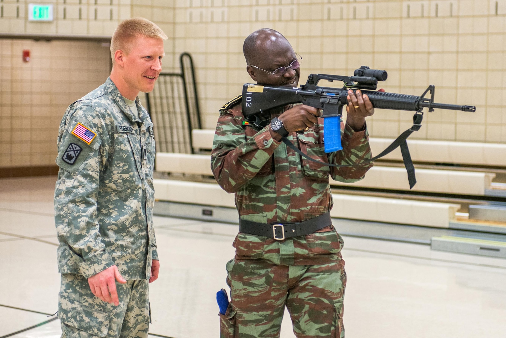 Capt Alan J. Roehrich, of the North Dakota Army National Guard’s 164th Regional Training Institute, assists Brig. Gen. Awal Nagnimi, Chief of Defense Forces for Benin (Forces Armees Beninois) in firing an M-16 rifle at the Guard’s Camp Grafton Training Center, near Devils Lake, North Dakota, on May 3, 2015. The M-16 is fitted with a training simulator called an “Ultimate Training Munition” that fires a paintball-type round for training. 