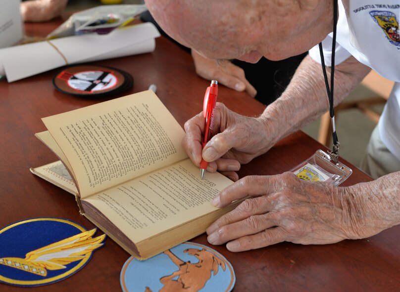 Retired Lt. Col.  Dick Cole signs a book at the Doolittle Raiders ceremony at Naval Air Station Pensacola May 8, 2015. Cole was honored at the ceremony, which commemorated the 80 men who flew B-25 Mitchell bombers over Tokyo after the Japanese attacked  Pearl Harbor. (U.S. Air Force photo/1st Lt. Ben Sowers)