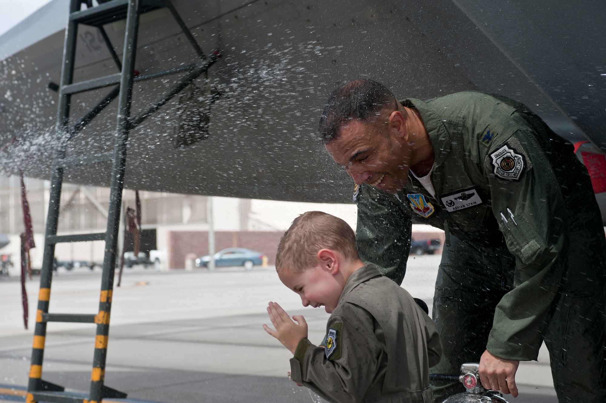 Col. Adrian Spain, U.S. Air Force Weapons School commandant, attempts to grab his son while being hosed down after his final flight as the USAFWS commandant at Nellis Air Force Base, Nev., May 11, 2015. It is tradition to dose the departing pilot with water upon their arrival back from their final flight. (U.S. Air Force photo by Staff Sgt. Siuta B. Ika)