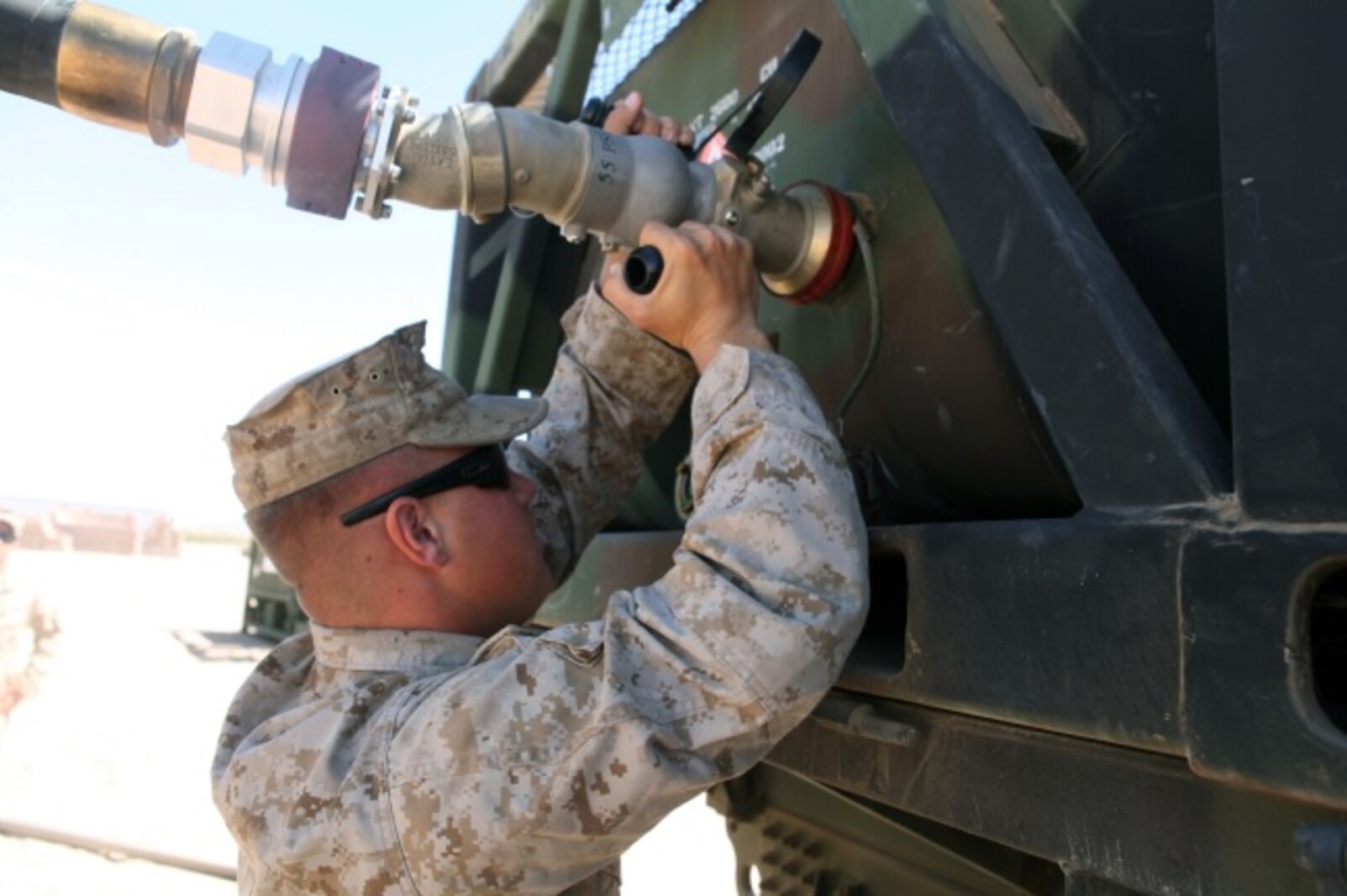 A Motor Transportation Operator with 1st Transport Support Battalion, Combat Logistics Regiment 1, 1st Marine Logistics Group, attaches a fuel hose to an AMK-23 Medium Tactical Vehicle Replacement with the help of two other Marines during routine refueling maintenance on the outskirts of Marine Corps Air Station Yuma, Ariz., April 10, 2015.
