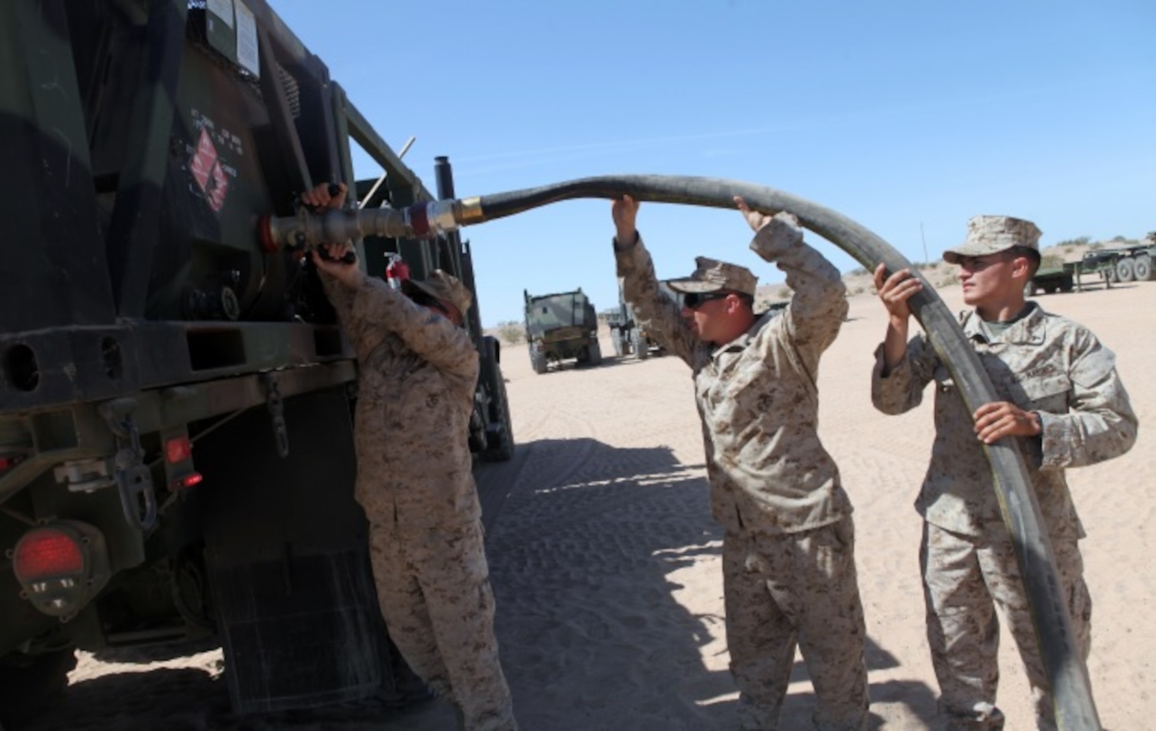 Private First Class Brenen Tischner, left, a Motor Transportation Operator, with 1st Transport Support Battalion, Combat Logistics Regiment 1, 1st Marine Logistics Group, attaches a fuel hose to an AMK-23 Medium Tactical Vehicle Replacement with the help of two other Marines during routine refueling maintenance on the outskirts of Marine Corps Air Station Yuma, Ariz., April 10, 2015.