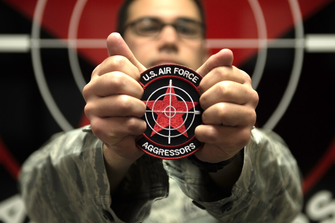 U.S. Air Force Staff Sgt. William Heines, 18th Aggressor Squadron baron controller, holds the unit patch which is adorned with its symbolic red star May 12, 2015, at Eielson Air Force Base, Alaska. The patch’s star and yellow hammer-and-sickle symbolizes the Soviet Union, the United States’ enemy during the Cold War. (U.S. Air Force photo by Staff Sgt. Shawn Nickel/Released)