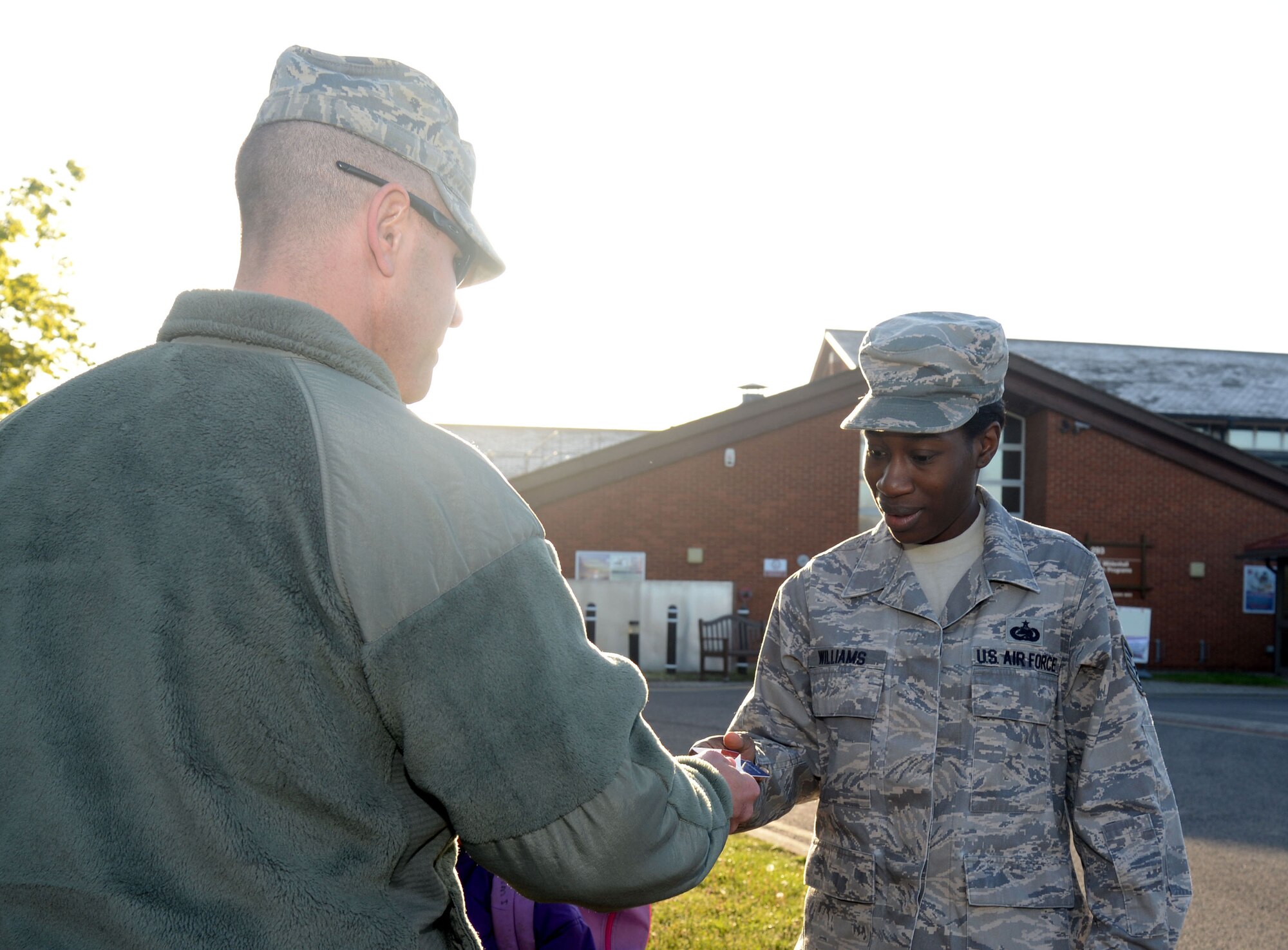 U.S. Air Force Master Sgt. Shane Gullick, left, 352nd Special Operations Support Squadron first sergeant from Memphis, Tenn., gives a $10 gift card to U.S. Air Force Tech. Sgt. Lasonja Williams, 352nd Special Operations Group NCO in charge of deployments from Savannah, Ga., May 13, 2015, as she drops her children off at the Child Development Center on RAF Mildenhall, England. Gullick, along with other Team Mildenhall first sergeants, have been choosing random locations to give out gift cards hoping to brighten others’ days with the new Random Acts of Kindness program. (U.S. Air Force photo by Senior Airman Kate Thornton/Released) 
