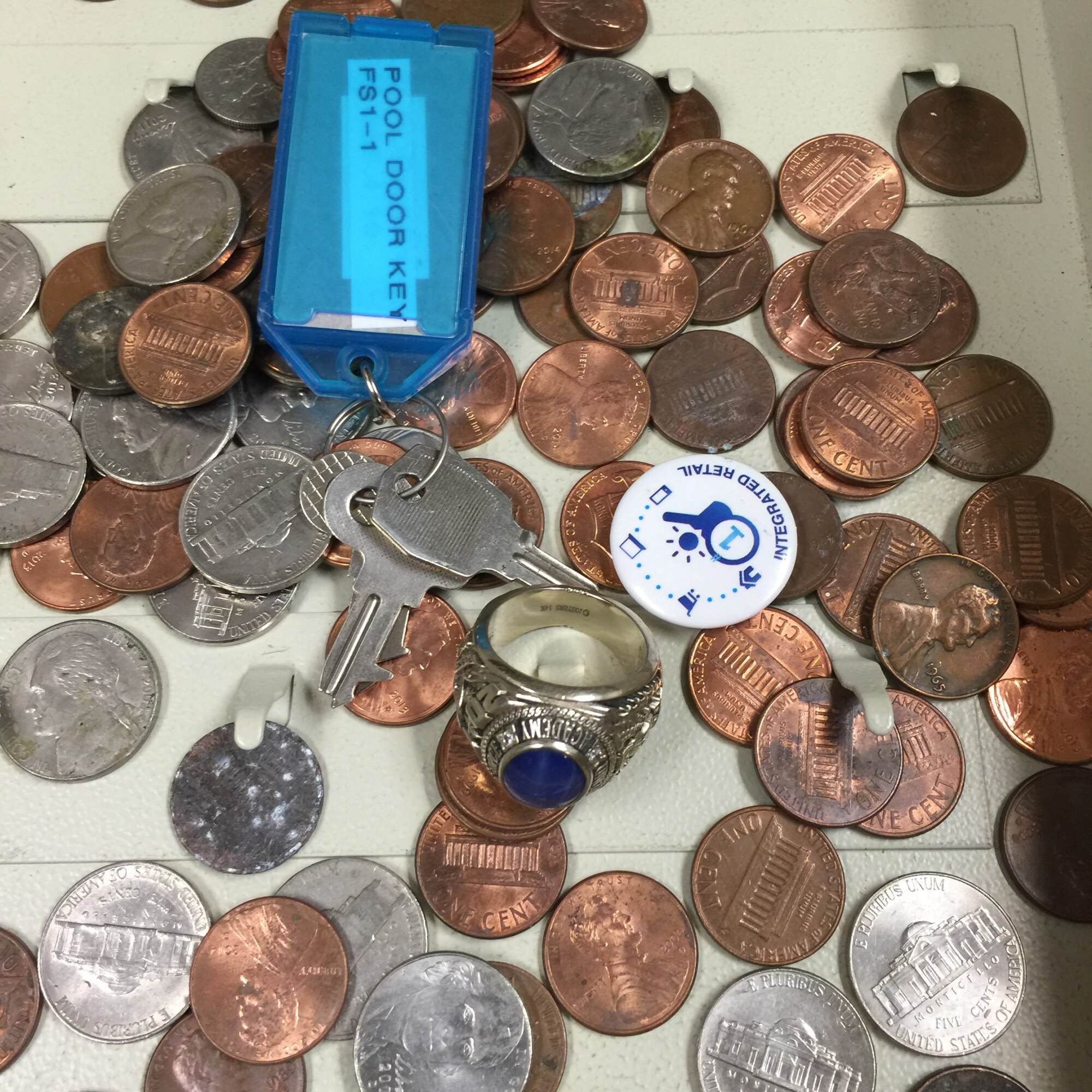 U.S. Air Force Capt. Joseph R. Lay’s 2005 Air Force Academy ring lays among the pile of items found in a combo locked metal cash box in the storage room at McGarr Pool during preparations for the 2015 pool season at Goodfellow Air Force Base, Texas, April 15, 2015. Lay, now a Flight Test Resources program manager at Eglin Air Force Base, Florida, lost the ring during a swimming lunch break in 2010. (Courtesy photo/ Released) 