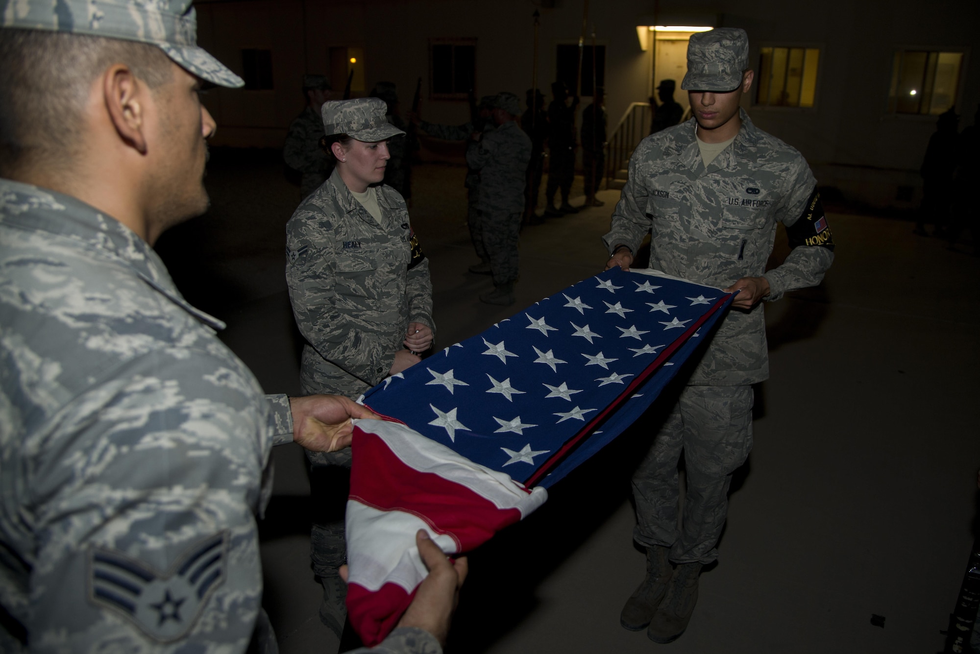 Senior Airman Enrique Caceres, 379th Expeditionary Civil Engineering Squadron, practices folding a flag during training with Airman 1st Class Nathaniel Jackson, 379th Expeditionary Aircraft Maintenance Squadron, while Airman 1st Class Samantha Healy, 379th Expeditionary Logistics Readiness Squadron, observes May 11, 2015, at Memorial Plaza on Al Udeid Air Base, Qatar. They train two days a week to practice and perfect their movements for any possible scenario while keeping their military bearing so they don't disrupt members in the audience during their details. (U.S. Air Force photo by Tech. Sgt. Douglas)