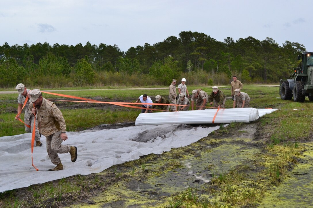 Rolling the mats out, staking them down, and then recovering the mats after they had been driven over multiple times proved to be quite challenging.  GySgt Damren and Cpl Regier pull the straps while the other Marines and contractors push the roll.     