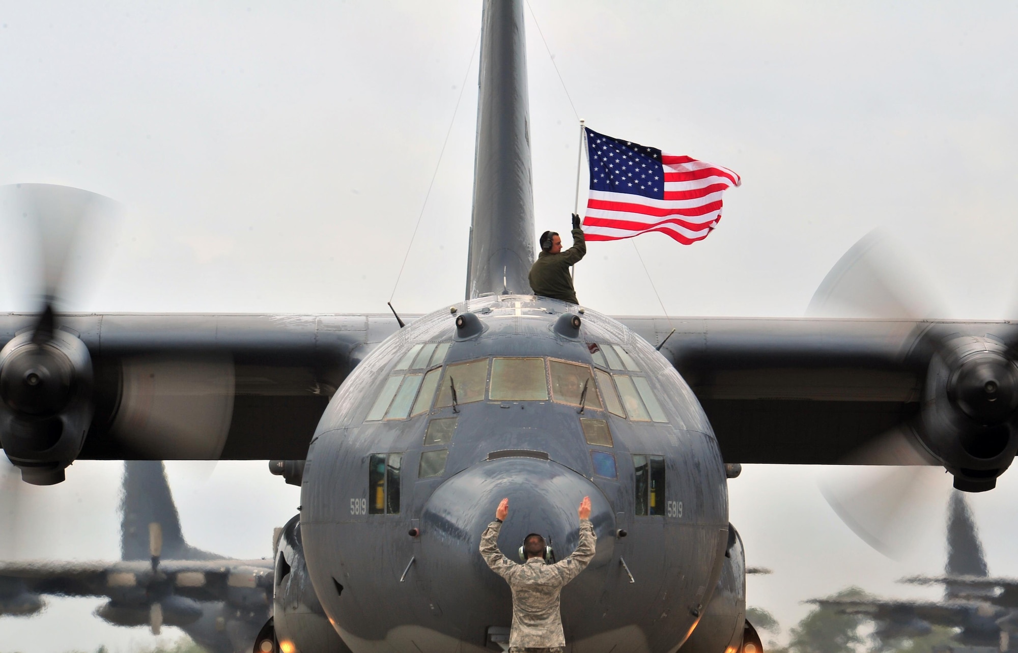 An aircrew member flies an American flag out of the top of an MC-130P Combat Shadow, May 15, 2015, at Hurlburt Field, Fla. The final two MC-130P Combat Shadow aircraft in the Air Force landed for the last time at Hurlburt Field, Fla., in front of more than 400 people and will take their last flight to the boneyard at Davis-Monthan Air Force Base, Arizona, June 1. (U.S. Air Force photo/Airman 1st Class Ryan Conroy) 