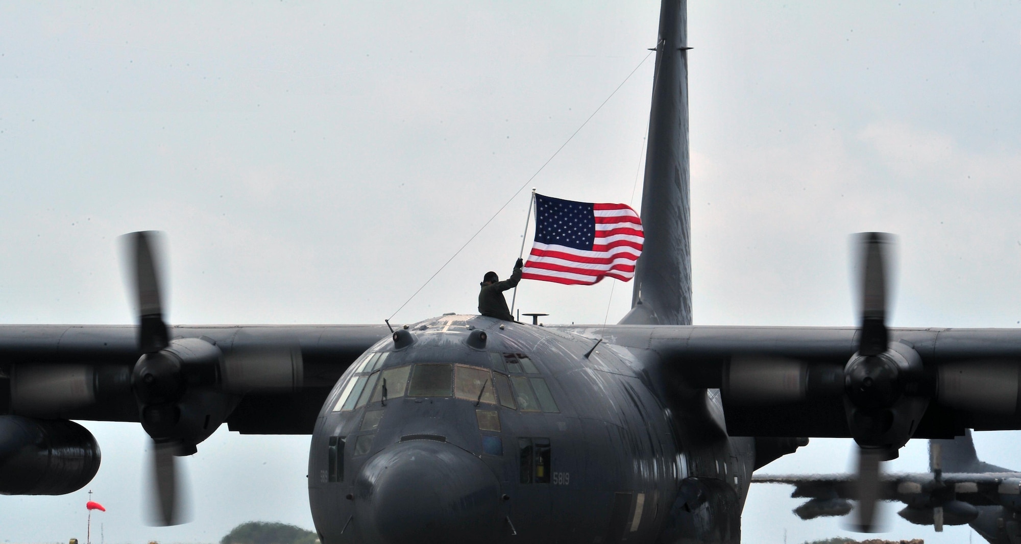 An aircrew member flies an American flag out of the top of an MC-130P Combat Shadow, May 15, 2015, at Hurlburt Field, Fla. Built with 1960s technology, the MC-130P began its special operations career in the mid-1980s and went on to conduct critical air refueling missions in the late 1980s during Operation Just Cause in Panama and the early 1990s during Operation Desert Storm. (U.S. Air Force photo/Airman 1st Class Ryan Conroy) 