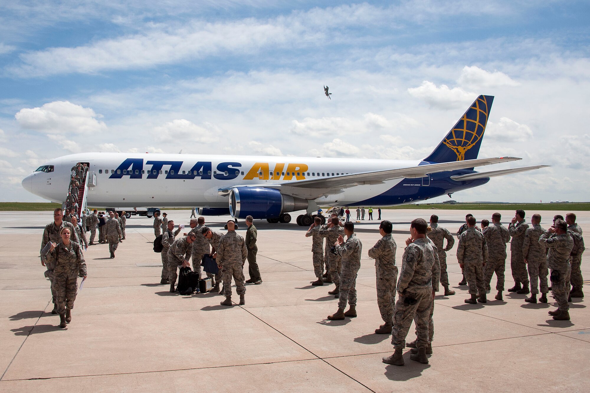 An F-16 fighting falcon flies overhead as members of the 140th Wing, Colorado Air National Guard, debark the plane that brought them home to Buckley AFB, Colo. May 15, 2015 after a 3-month deployment to the Republic of Korea. The unit sent the jets and associated personnel to Korea as part of a Theater Security Package, to train with allied partners and strengthen ties with international partners.  (U.S. Air National Guard photo by Senior Master Sgt. John Rohrer) 