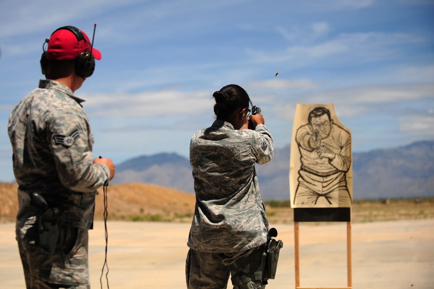 U.S. Air Force Staff Sgt.  Maeve Kaneakalau, 355th Security Forces member, fires her weapon at a target as Senior Airman Ethan Talbot, 355th SFS combat arms instructor, observes during the practice round of a firing competition in honor of National Police Week at Davis-Monthan Air Force Base, Ariz., May 13, 2015. National Police Week pays special recognition to law enforcement officers who have lost their lives in the line of duty. (U.S. Air Force photo by Airman 1st Class Chris Drzazgowski/Released) 