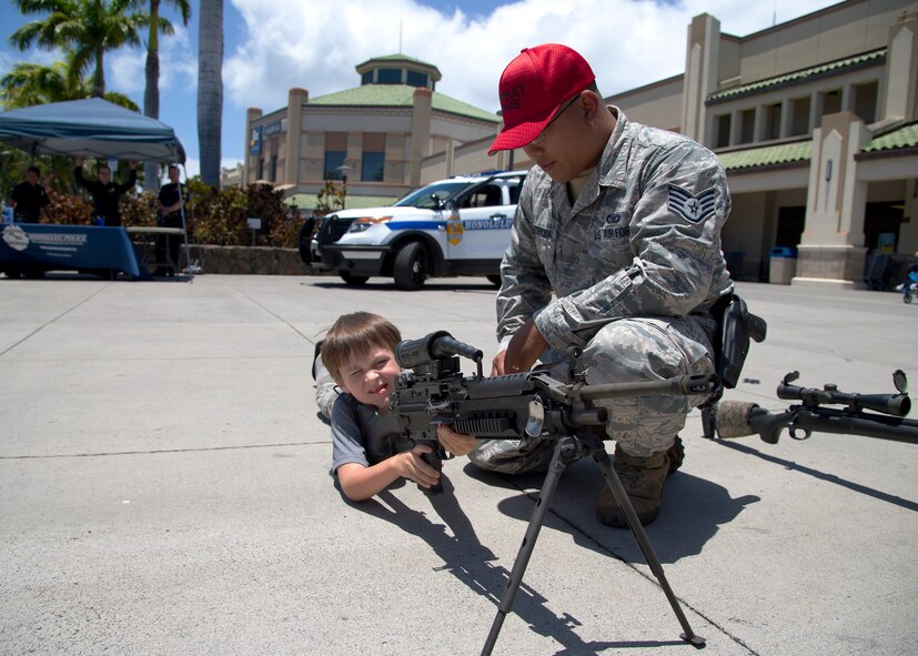 Staff Sgt. Dean Concepcion, 647th Security Forces Squadron combat arms instructor, shows  Hayven the M249 weapon system during  the National Police Week fair at the Navy Exchange Mall, Hawaii, May 13, 2015. In 1962, President John F. Kennedy signed a proclamation which designated May 15 as Peace Officers Memorial Day and the week in which that date falls as Police Week. (U.S. Air Force photo by Tech. Sgt. Aaron Oelrich/Released) 