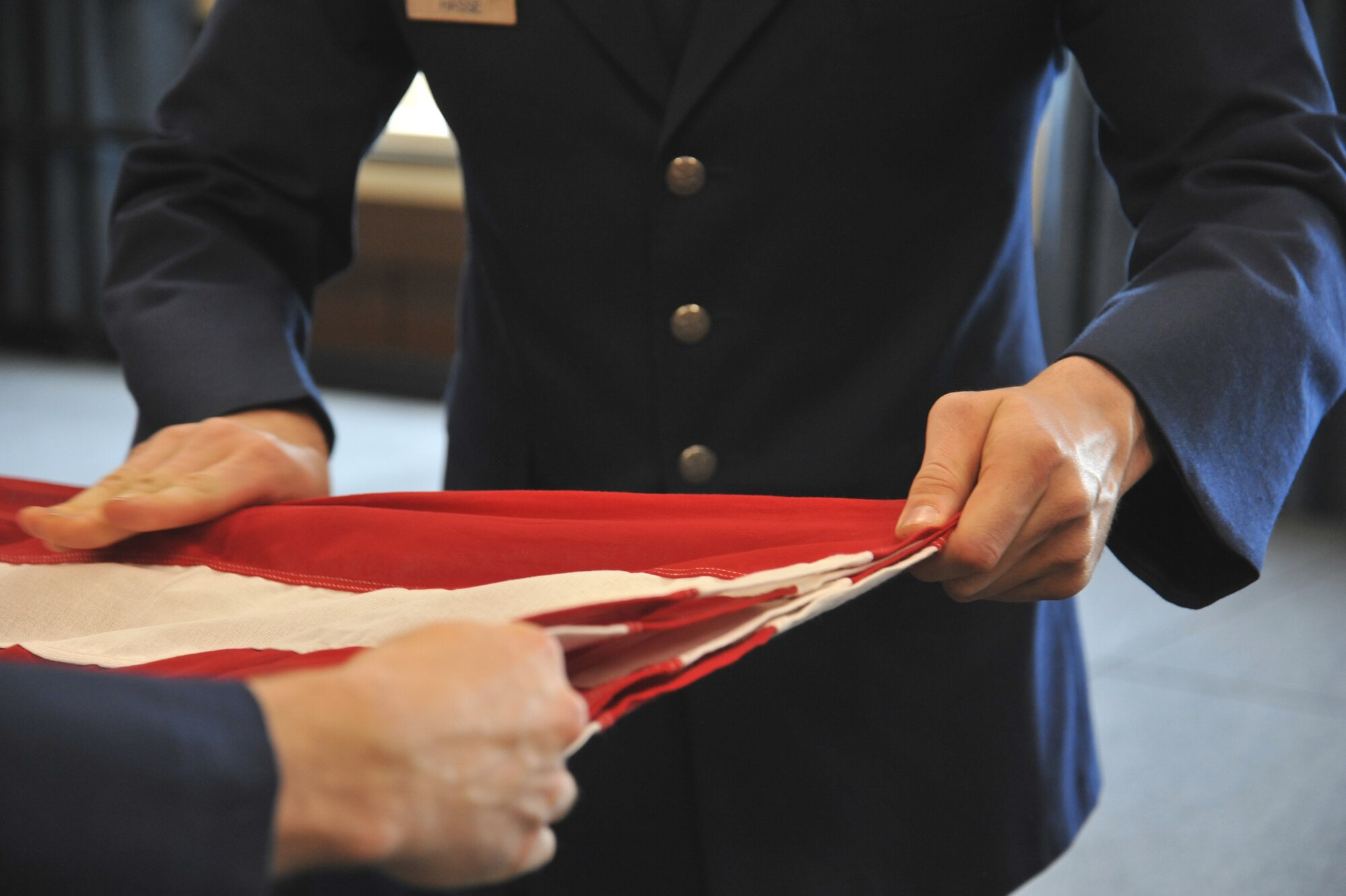 Senior Airman Marcus Hasse, 92nd Aircraft Maintenance Squadron integrated flight controls system journeyman, smooths out the American flag during a six-man flag fold during his Honor Guard graduation May 15, 2015, in the Red Morgan Center at Fairchild Air Force Base, Wash. The body bearers element participates in U.S. Air Force, joint service and state funerals by carrying the remains of deceased service members and their dependents to their final resting places. (U.S. Air Force photo/Staff Sgt. Samantha Krolikowski)