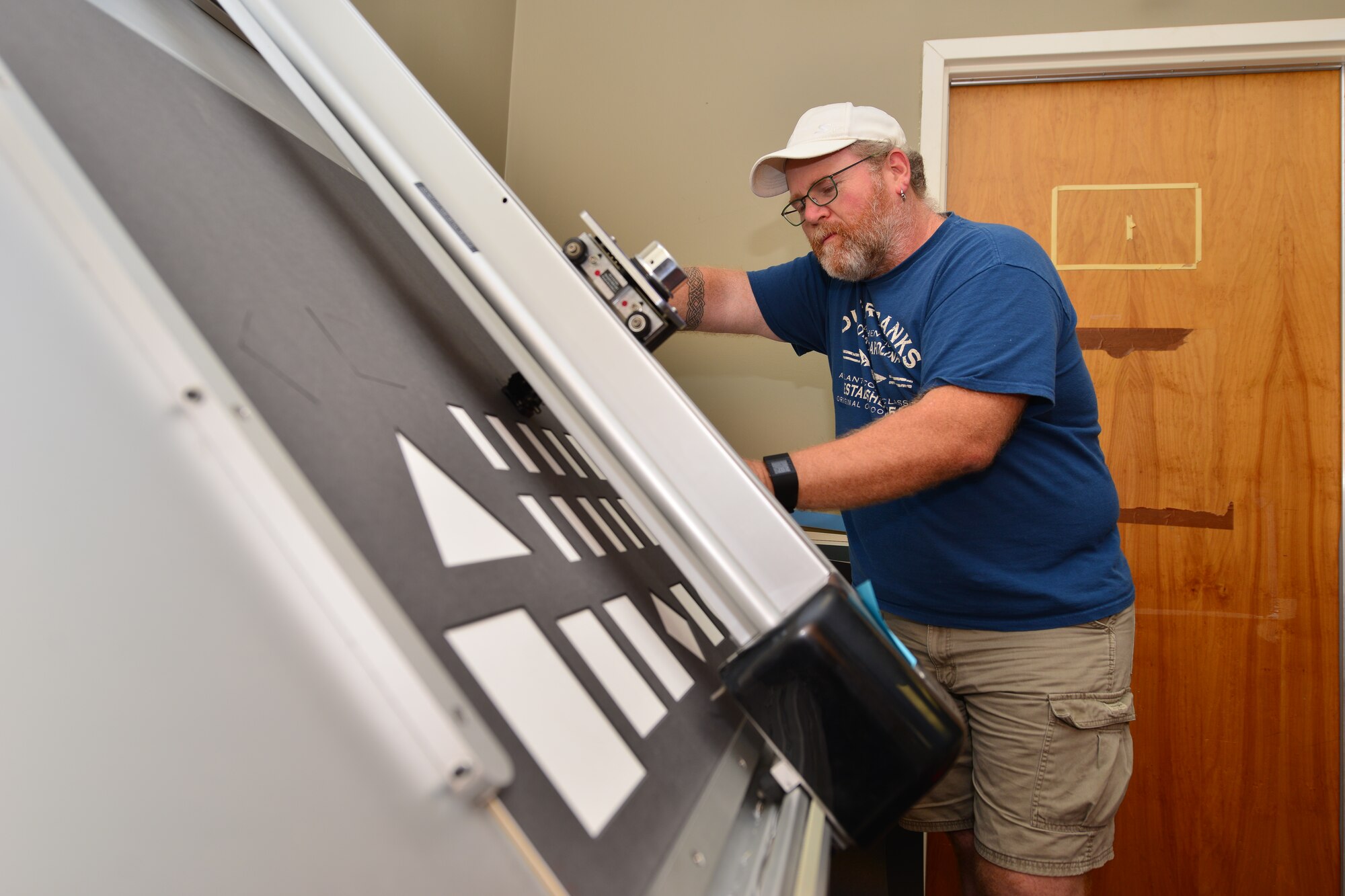 Mark Winslow, 733rd Mission Support Division Morale, Welfare and Recreation frame shop technician, holds matting in place as an automatic matte cutter slices shapes for a shadow box at Fort Eustis, Va., May 12, 2015. Winslow input a design on a computer which was then sent to the cutter to perform. (U.S. Air Force photo by Staff Sgt. Natasha Stannard/Released)
