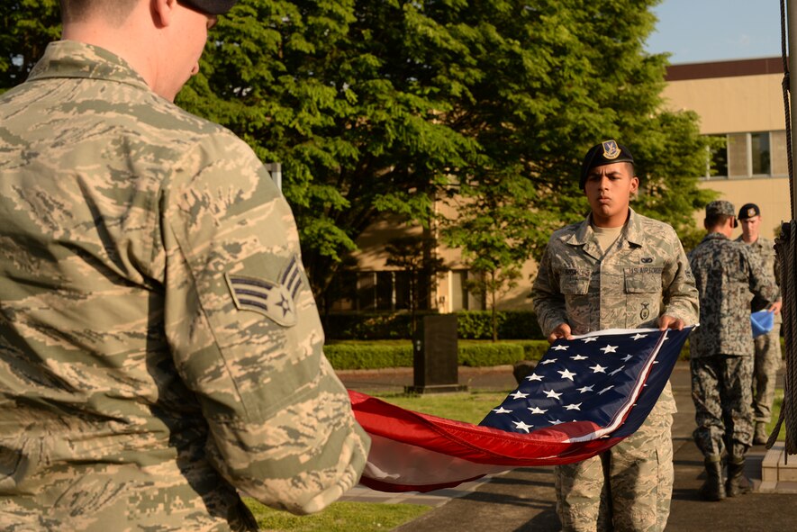 374th Security Forces Squadron patrolmen, Senior Airman David Wells and Airman 1st Class Nelson Sosa, fold the U.S. flag during a retreat ceremony held during Police Week at Yokota Air Base, Japan, May 13, 2015. Police Week events included a 5K run, a physical fitness challenge, displays in front of the Yokota Community Center and a Policeman's Ball.  (U.S. Air Force photo by Airman 1st Class Elizabeth Baker/Released)