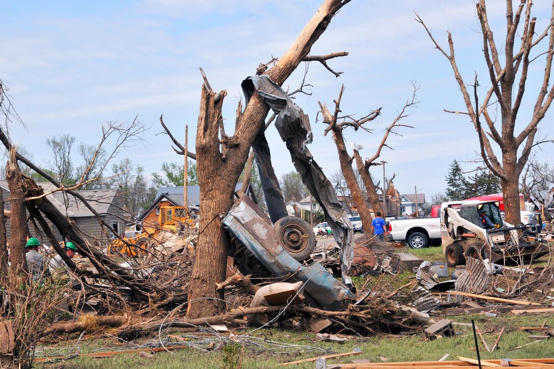 A mangled vehicle leans against tree as airmen and residents clear debris during tornado recovery efforts in Delmont, S.D., May 12, 2015.  
