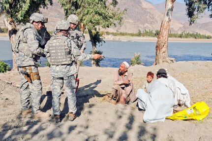 Air Force Chief Master Sgt. Don Kuehl (left), Air Force Staff Sgt. Bennett Groth and an interpreter talk with three farmers planting alfalfa at the proposed site of a demonstration farm near the Sarkani District Center in Kunar province, Nov. 22.