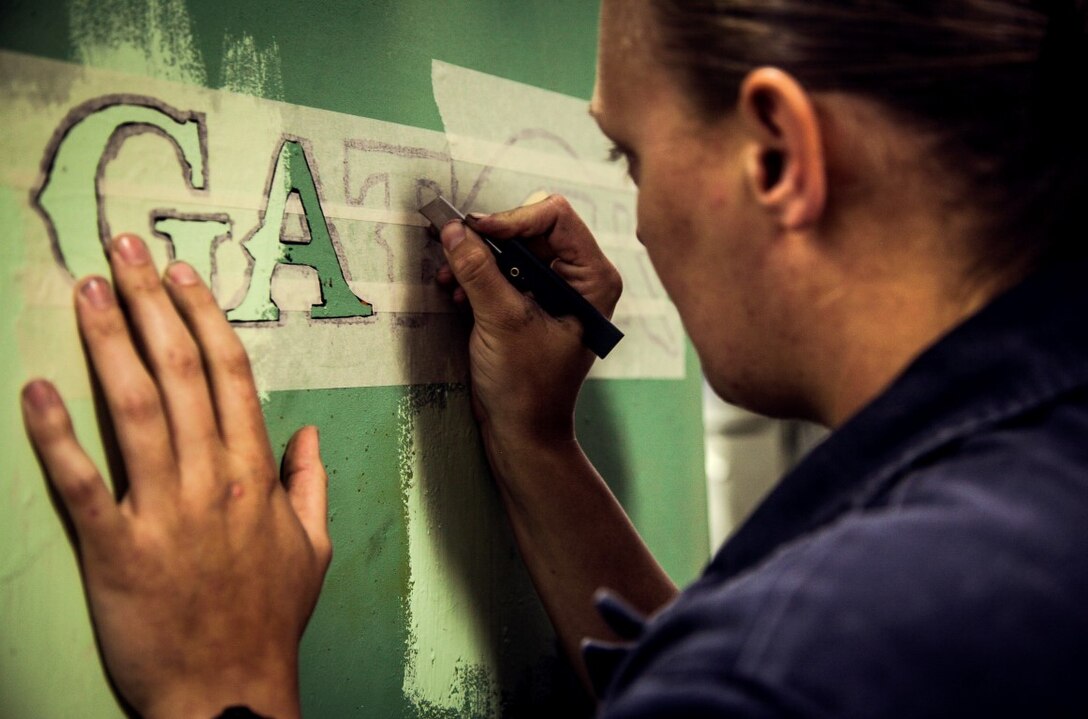 U.S. Navy Aviation Support Equipment Technician Airman Christine Lachico stencils a logo on equipment in the hangar bay of the USS Essex (LDH 2) at sea in the Pacific Ocean, May 16, 2015. Lachico is part of aviation ground support equipment element with the Essex Amphibious Ready Group, embarked on a seven-month deployment.  (U.S. Marine Corps photo by Cpl. Elize McKelvey/Released)