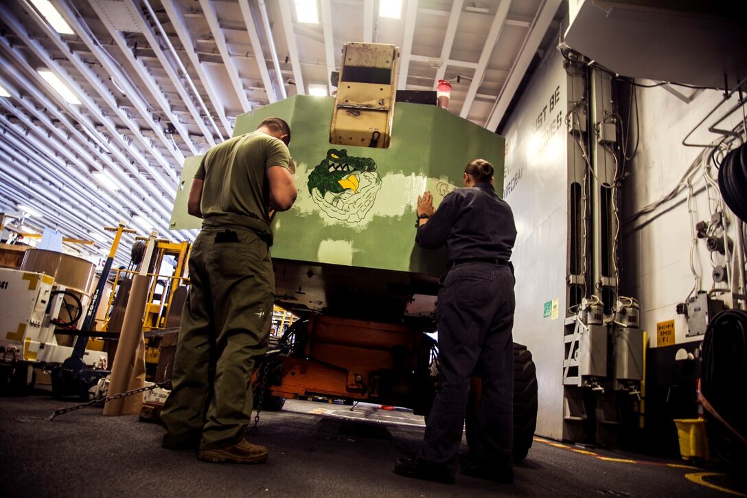 U.S. Marine Cpl. Zachary Maples and Navy Aviation Support Equipment Technician Airman Christine Lachico paint a logo on equipment in the hangar bay of the USS Essex (LDH 2) at sea in the Pacific Ocean, May 16, 2015. Both Maples and Lachico are part of aviation ground support equipment elements with the 15th Marine Expeditionary Unit and the Essex Amphibious Ready Group, embarked on a seven-month deployment.  (U.S. Marine Corps photo by Cpl. Elize McKelvey/Released)