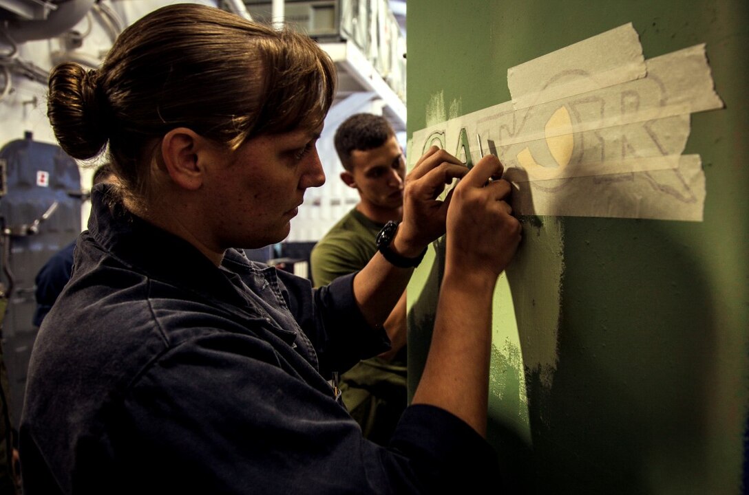 U.S. Navy Aviation Support Equipment Technician Airman Christine Lachico, left, and Marine Cpl. Zachary Maples paint a logo on equipment in the hangar bay of the USS Essex (LDH 2) at sea in the Pacific Ocean, May 16, 2015. Both Maples and Lachico are part of aviation ground support equipment element with the 15th Marine Expeditionary Unit and the Essex Amphibious Ready Group, embarked on a seven-month deployment.  (U.S. Marine Corps photo by Cpl. Elize McKelvey/Released)