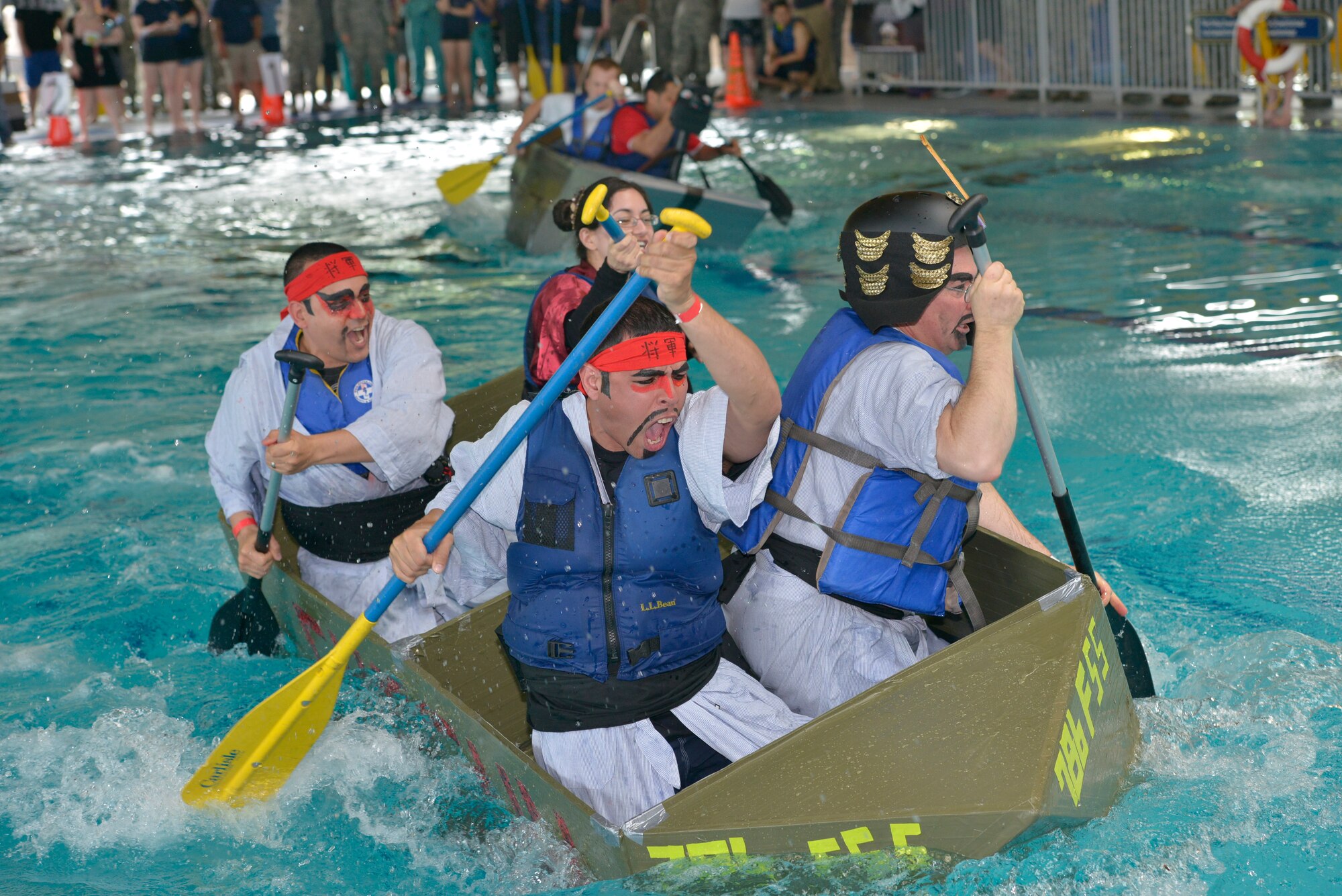 Participants from the 786th Force Support Squadron paddle pass the other teams during the Battle of the Battleships competition May 15, 2015, at Ramstein Air Base, Germany. The competition began with boat races, where teams were tasked to pedal their custom-built boats from one end of the pool to the other as quickly as possible. (U.S. Air Force photo by Airman 1st Class Lane T. Plummer/Released)