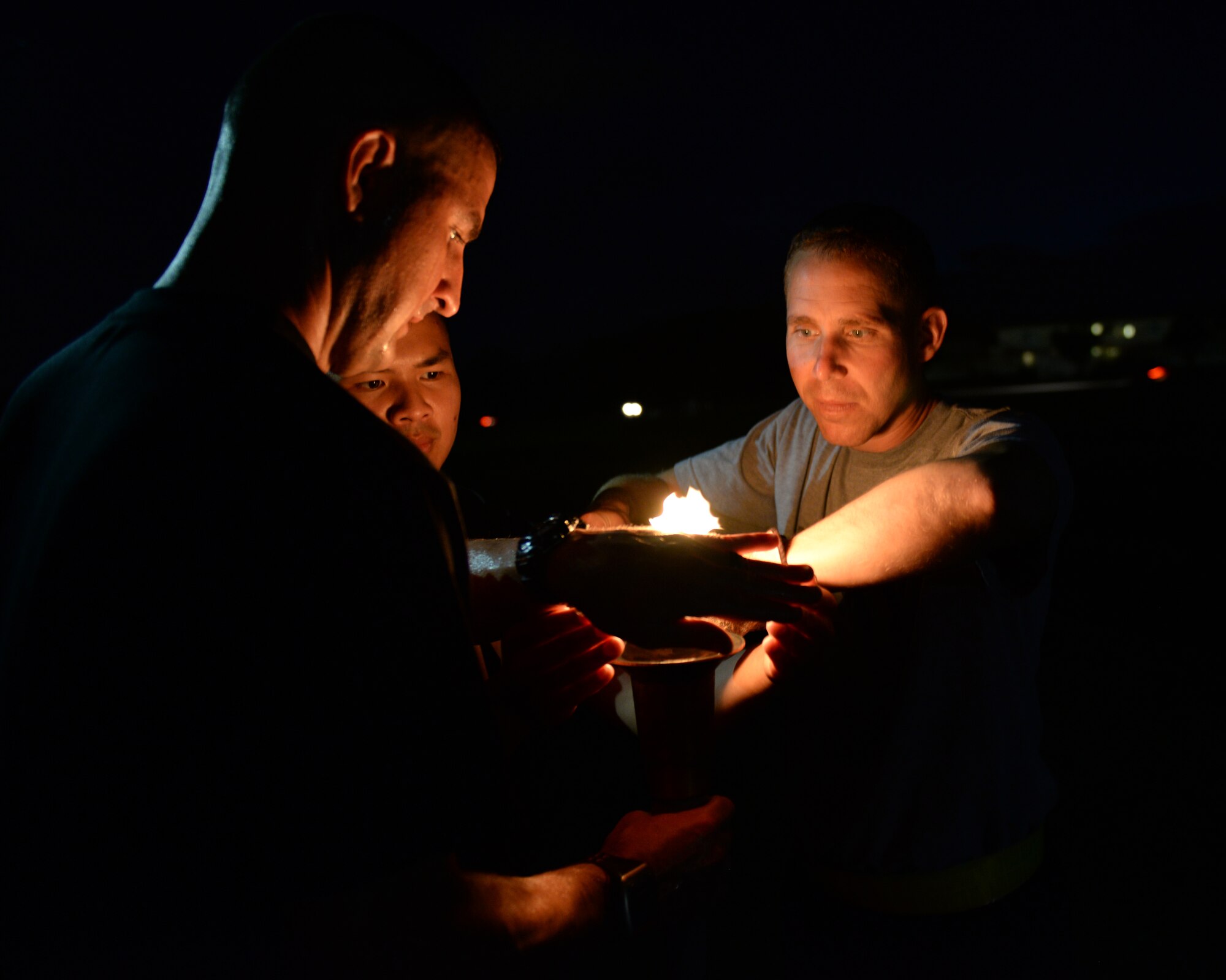 U.S. Army Capt. Nathan Elkins, 247th Military Police Detachment commander, Sgt. 1st Class Robert Cree, 247th MPD first sergeant, and Staff Sgt. Nho Nguy, 247th MPD desk sergeant, relight a torch for the National Police Week 24-hour vigil run on Kadena Air Base, Japan, May 15, 2015. Multiple law enforcement personnel from different services came together in a joint effort to support National Police Week. (U.S. Air Force photo by Senior Airman Omari Bernard)