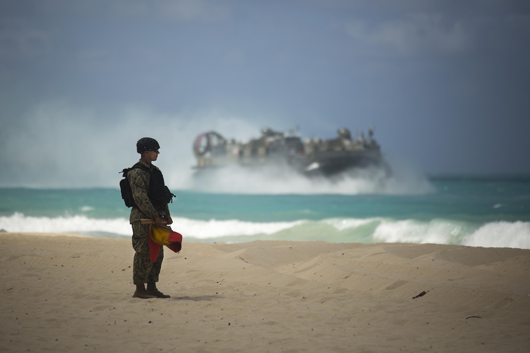 A U.S. Navy service member stands on the beach as a Landing Craft Air Cushion prepares to breach the shore during the MARFORPAC-hosted U.S. Pacific Command Amphibious Leaders Symposium (PALS) at Marine Corps Training Area Bellows May 19, 2015. The objective of PALS is to have meaningful dialogue on key aspects of maritime and amphibious operations, capability development, and interoperability. (U.S. Marine Corps photo by Cpl. Matthew J. Bragg)