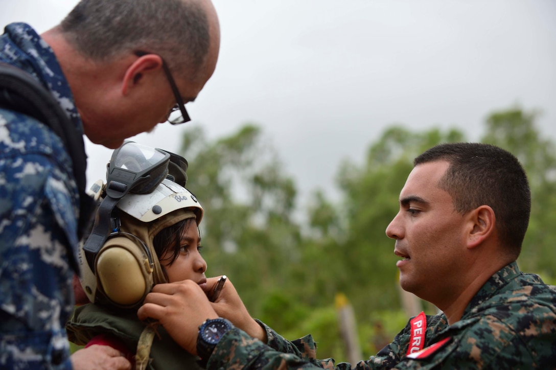 U.S. Navy Capt. Miguel Cubano, left, and Peruvian Navy Lt. Roberto Nieto assist a Nicaraguan citizen with putting on a helmet before boarding a helicopter during Continuing Promise 2015 in Puerto Cabezas, Nicaragua, May 17, 2015. Cubano is the executive officer of the military treatment facility on the hospital ship USNS Comfort and Nieto is currently attached to Commander, Destroyer Squadron 40, the command element for CP 15.