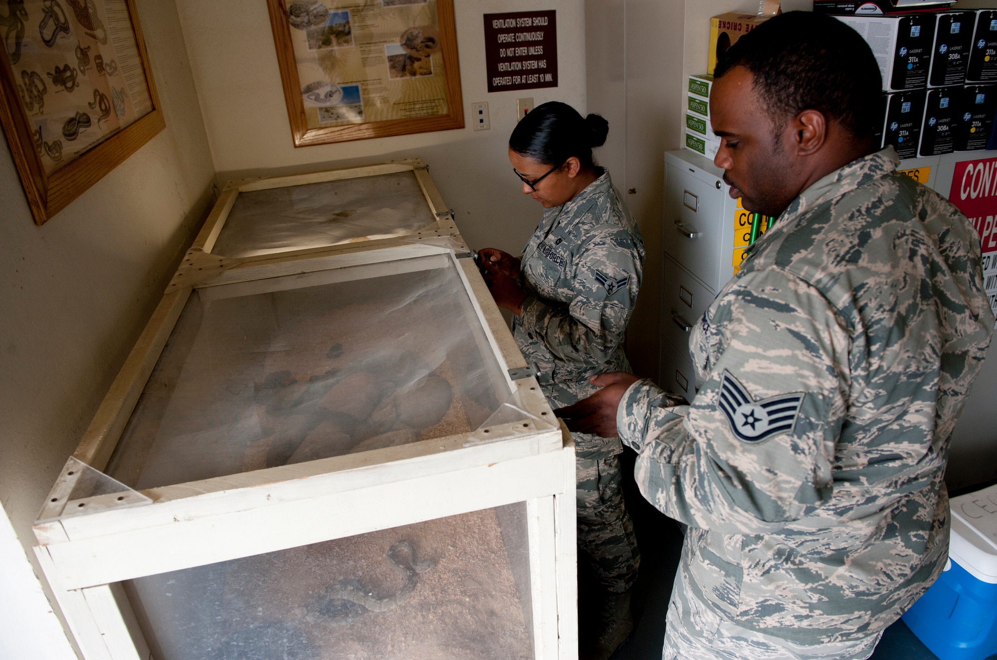 Staff Sgt. Robert Williams and Airman 1st Class Taylor Bradford, 49th Civil Engineer Squadron pest management, unlock the tank to the three species of rattlesnakes they shelter in their facility at Holloman Air Force Base, N.M. May 14, 2015. The snakes were relocated to the facility from rescues around base and are used as a training tool for the members to learn how to properly handle the snake, ensuring safety of personnel as well as safety for the snakes. (U.S. Air Force photo by Senior Airman Leah Ferrante/released)