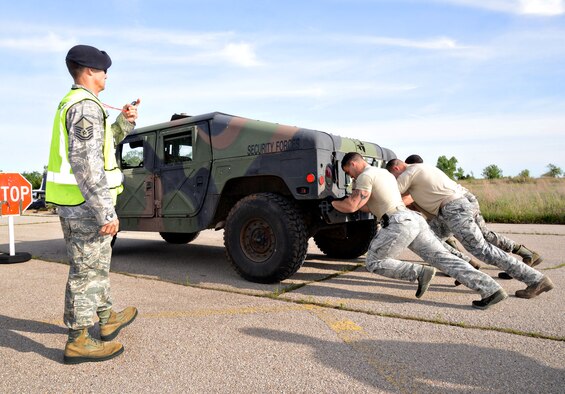 Master Sgt. Matthew Gioielli starts the timer for one of the teams competing in the Defender Games’ 1.5K gauntlet obstacle course May 12. The four-person teams worked together to push a humvee uphill for 50 meters (as shown), fill sandbags, flip tires, do 20 Burpees, carry weighted ammo boxes, carry dummies to the next checkpoint, then carry 5 gallon jugs, all while trying to remember items in a box they had previously observed. This team consisted of Senior Airman Christopher Loveland, Staff Sgt. Cacy Wyatt, Staff Sgt. Bon Albana and Senior Airman Aaron Gray. (Air Force photo by Kelly White/Released)
