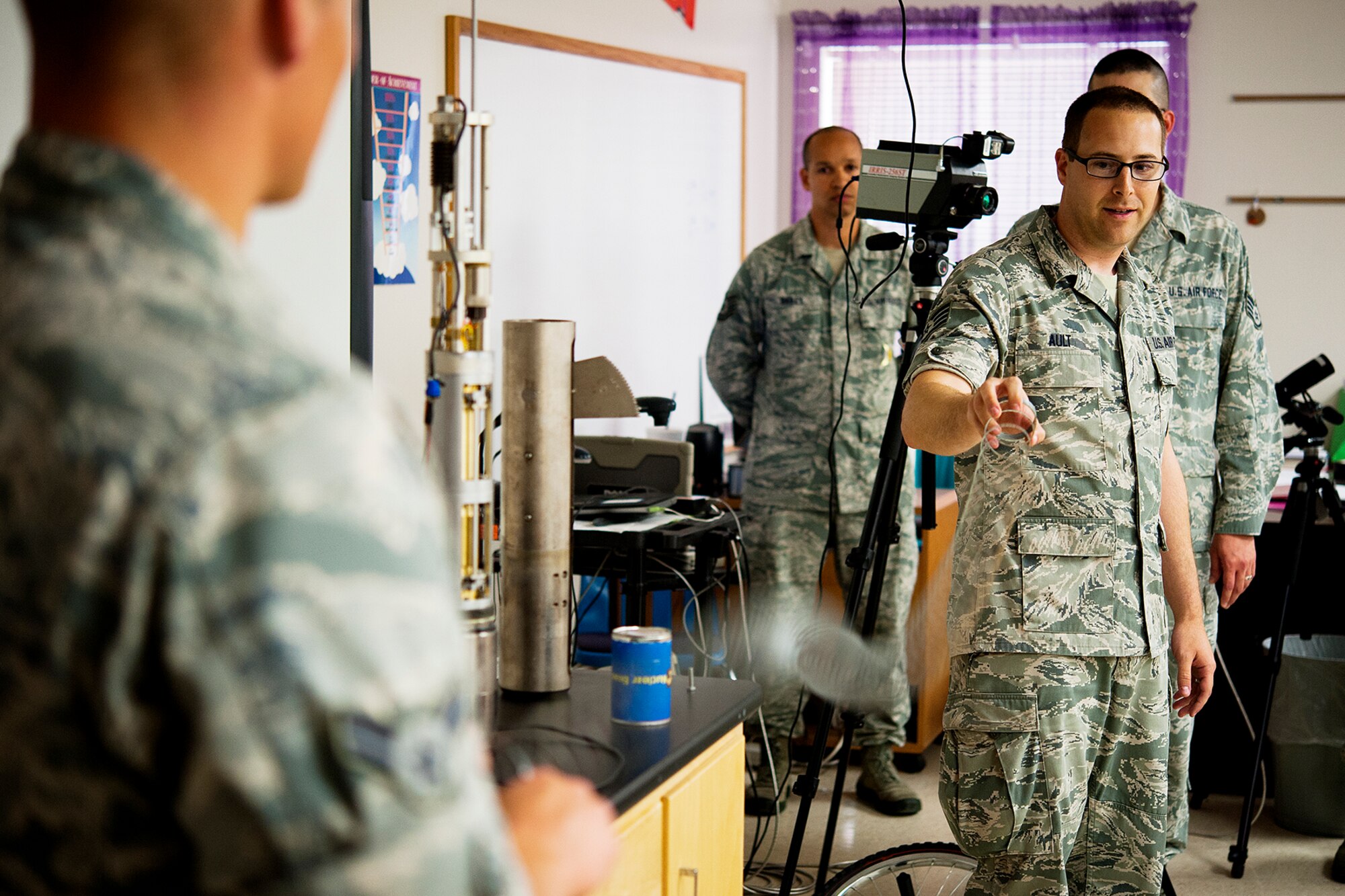 U.S. Air Force Staff Sgt. James D. Ault, 312th Training Squadron instructor, right, and Airman 1st Class Christopher E. Krause, 312th TRS student, left, wave a Slinky at Lee Middle School in San Angelo, Texas, May 19, 2015. Ault and Krause showed 8th grade students how a seismometer is used to measure motion of the ground and used the Slinky to explain the difference between compression rarefaction, transverse and elliptical retrograde waves. (U.S. Air Force photo by Airman 1st Class Devin Boyer/Released)