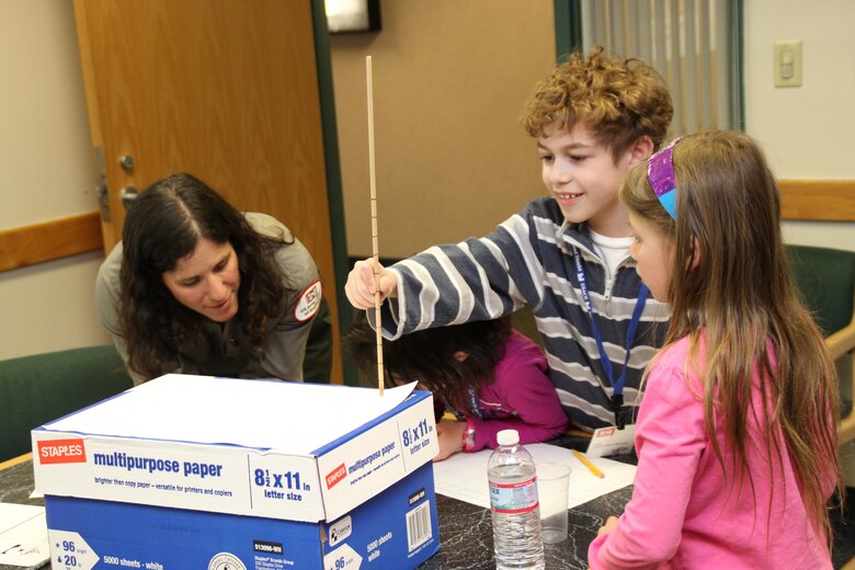 Children measure the imaginary bottom of the seafloor using a paper box and wooden measuring instrument.