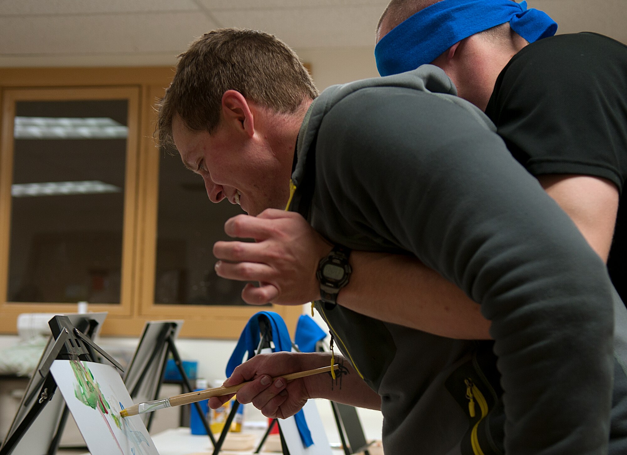 Staff Sgt. Ben Hebert directs Airman 1st Class Joseph Lunt’s hand in an attempt to paint a picture May 20, 2015, during the 90th Force Support Squadron’s Amazing Race competition. Three teams of three Airmen competed in a race across base, performing a number of different tasks at each location. (U.S. Air Force photo by Airman 1st Class Brandon Valle)