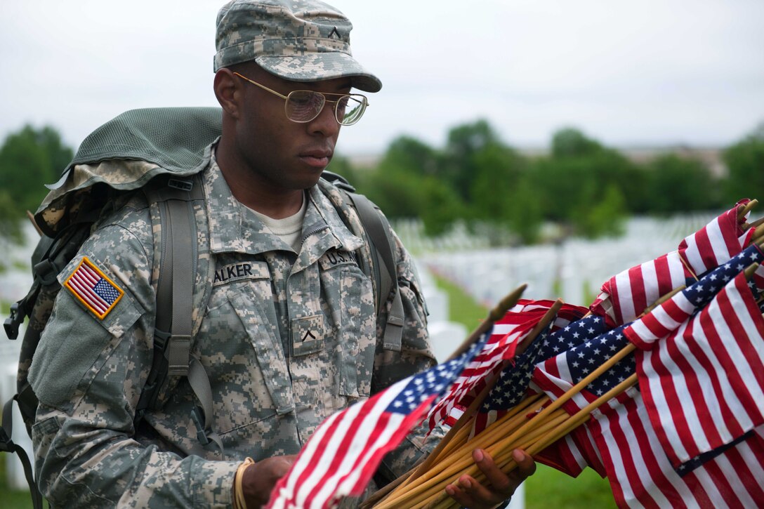Army Pvt. Tim Walker places small American flags into the ground in front of headstones in Section 64 during “Flags In” at Arlington National Cemetery in Arlington, Va., May 21, 2015. Walker is assigned to the 3rd U.S. Infantry Regiment, known as "The Old Guard."