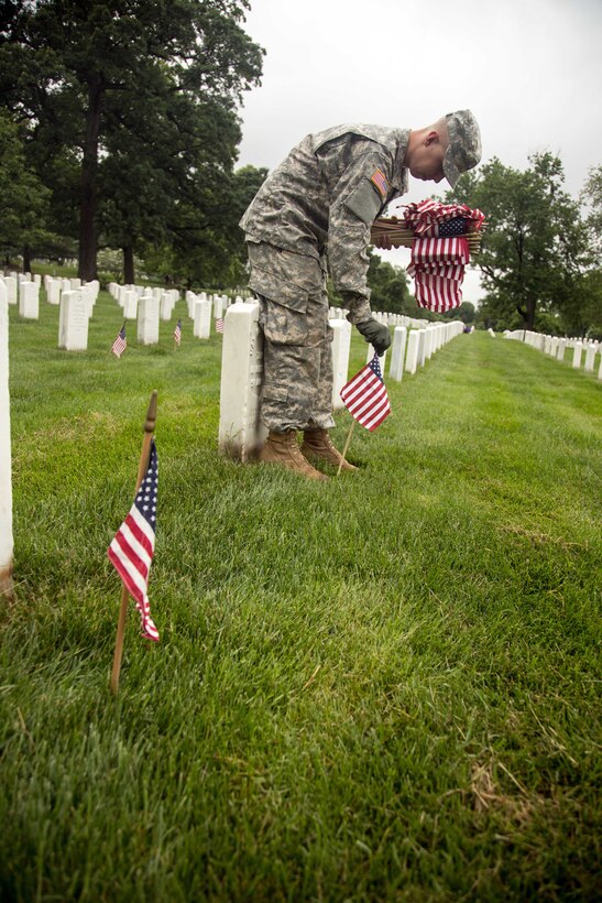 A soldier places a small American flag in front of a marker during “Flags In” at Arlington National Cemetery in Arlington, Va., May 21, 2015.