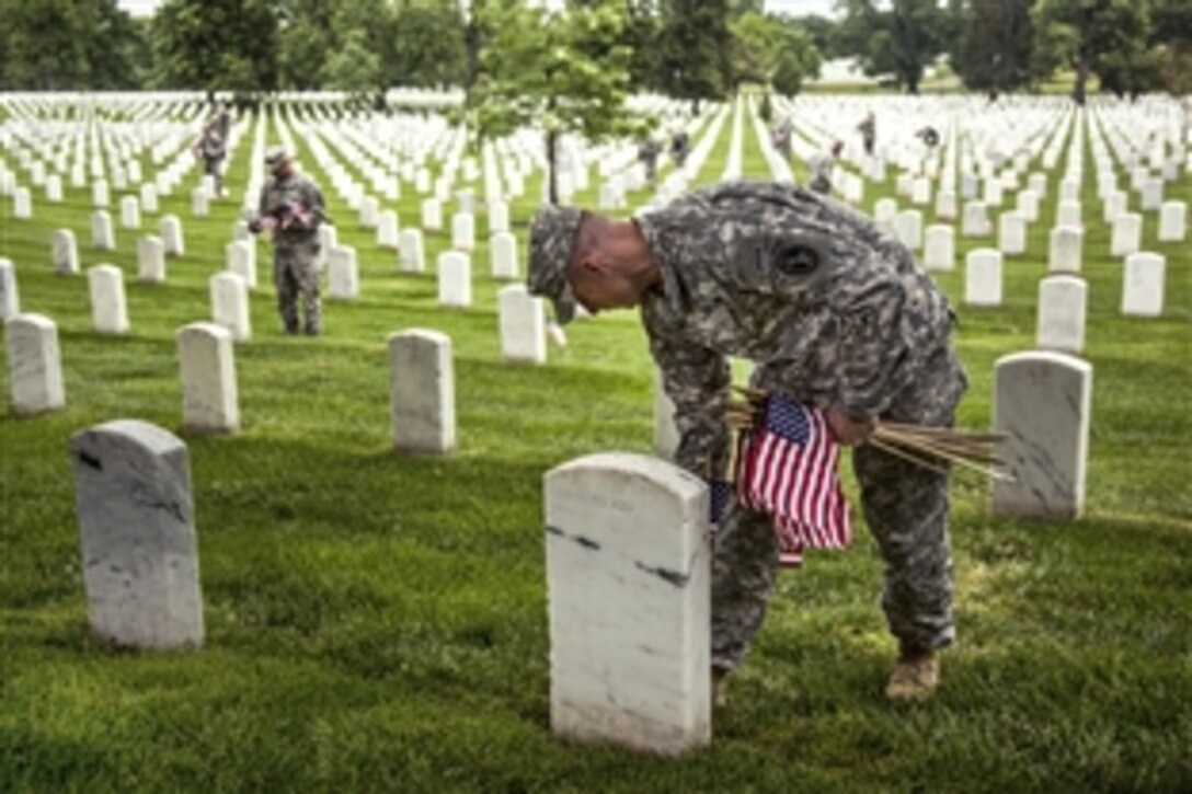 A soldier places a small American flag into the ground in front of a headstone during “Flags In” at Arlington National Cemetery in Arlington, Va., May 21, 2015. During the annual tradition before Memorial Day, soldiers assigned to the 3rd U.S. Infantry Regiment, known as “The Old Guard,” place small American flags next to 228,000 headstones.