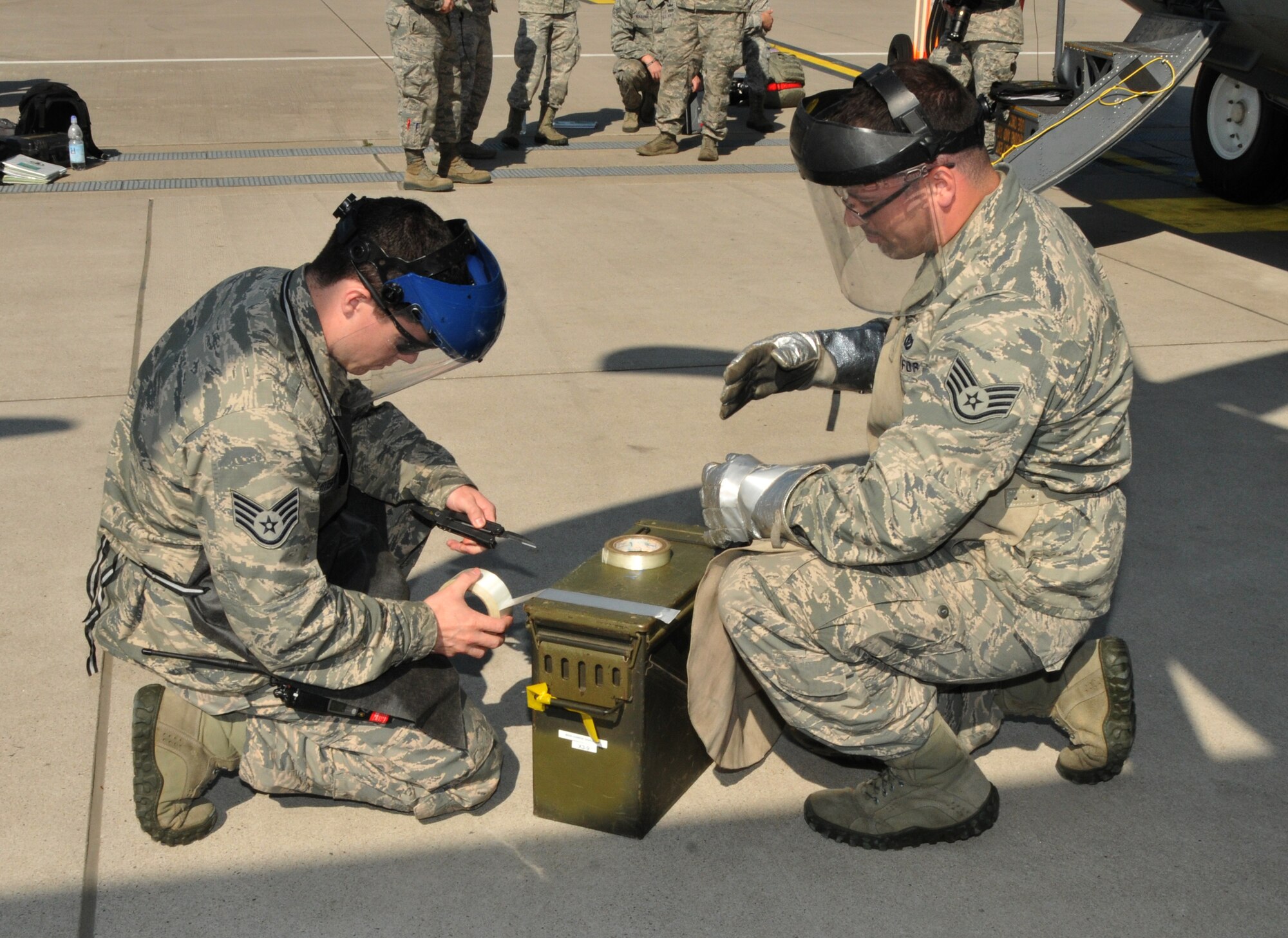 The non-commissioned officer in charge of equipment, and the non-commissioned officer in charge of operations, 104th Explosive Ordnance Flight (EOD), 104th Fighter Wing, Barnes Air National Guard Base, Westfield, Mass., cut duct tape to secure flares to safe the C-130 aircraft, May 13, 2015, Ramstein, Air Base Germany. The Airmen are emergency responders who will be qualified on “Safeing” the C-130 aircraft, making him more valuable to the 104th Fighter Wing and New England area. (U.S. Air National Guard photo by Tech. Sgt. Melanie J. Casineau/Released)